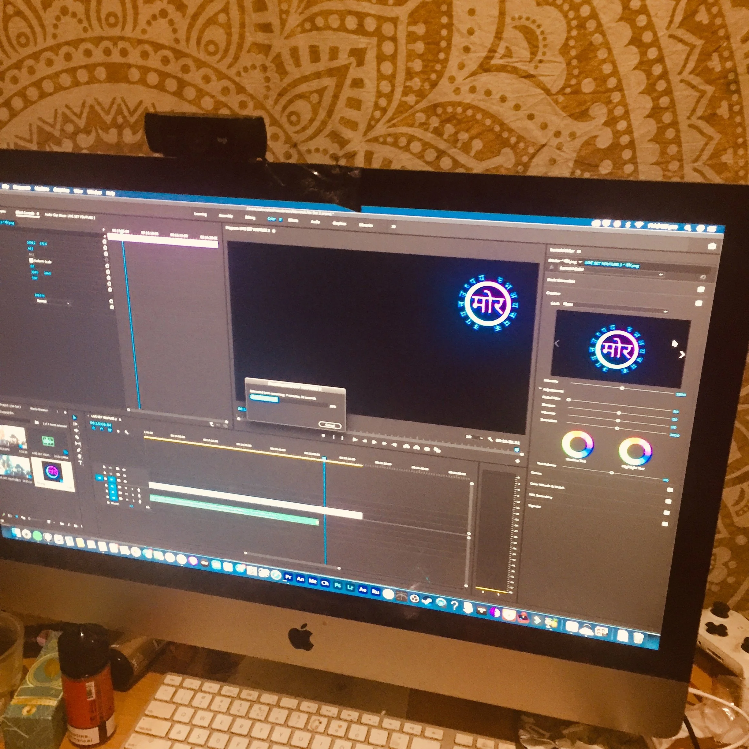 Computer screen displaying video editing software with a colorful logo in the center. The workspace includes tools, timelines, and media bins. The background shows a brown decorative wall with patterns.