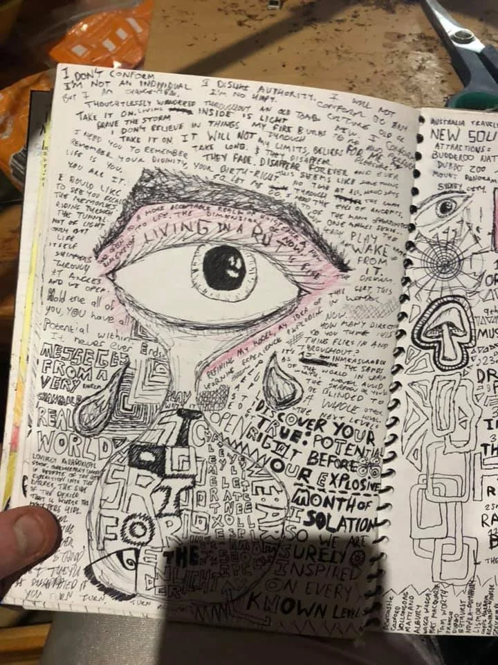A handwritten page with sketches and notes. It features a large eye drawn at the center, with a tear falling down, surrounded by various doodles and abstract shapes. The text discusses themes of living in the moment, self-discovery, and inspiration.