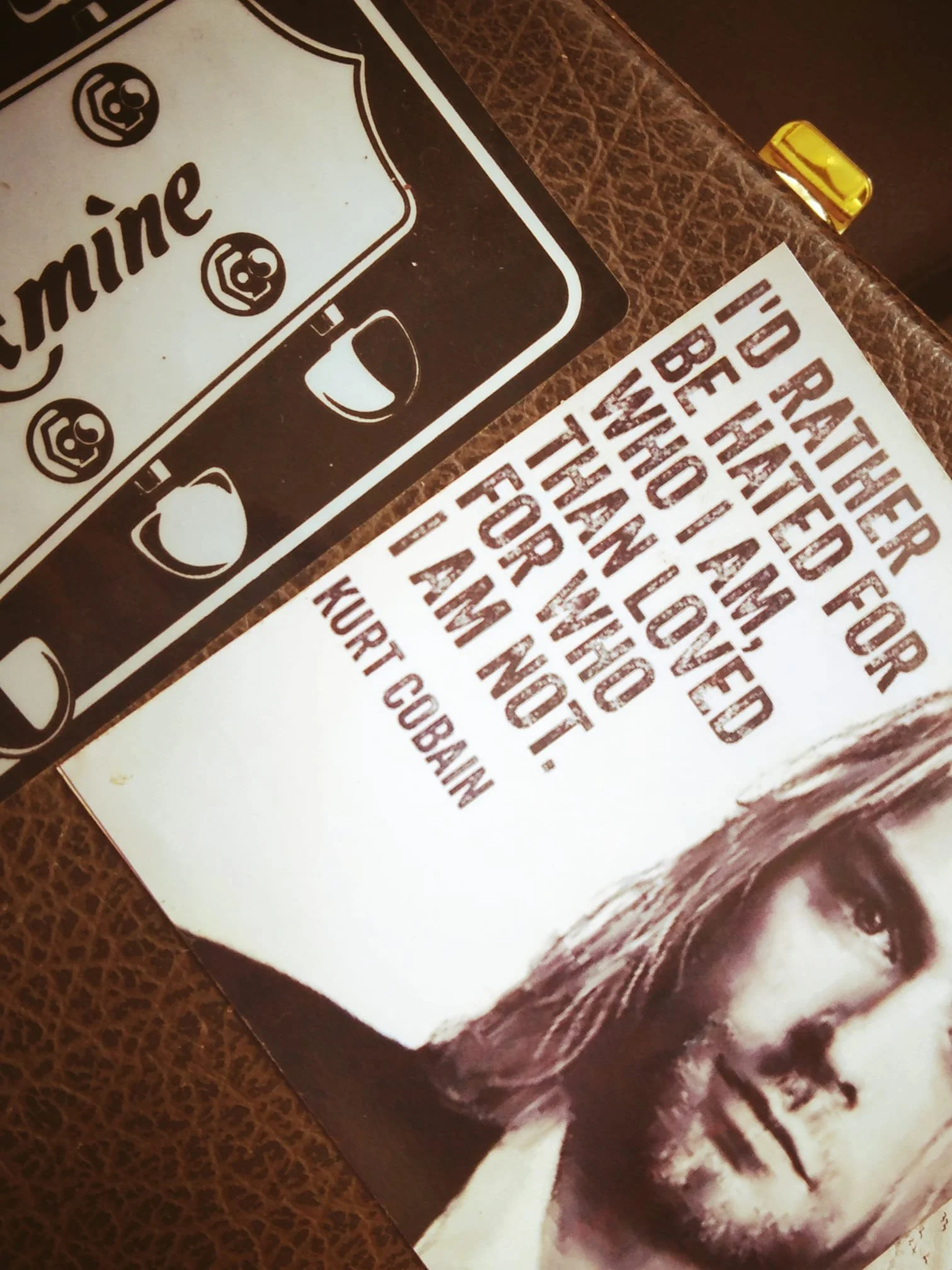 A printed quote by Kurt Cobain that reads, "I'd rather be hated for who I am than loved for who I am not." A black and white sticker or sign with a skull and crossbones design partially displayed in the image.
