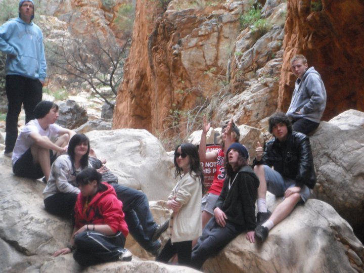 Group of young people sitting and standing on rocks in a canyon or desert landscape.