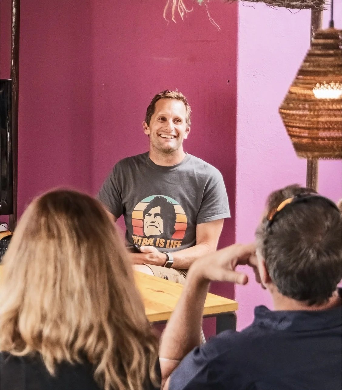 Richard Clarke, Man smiling while speaking to a group of people in a room with purple walls, sitting at a table.