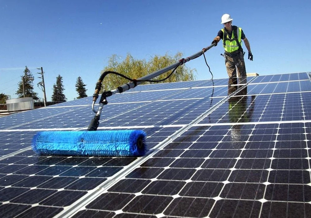 A man cleans solar panels with a brush, enhancing efficiency by removing dirt and debris for optimal energy production.