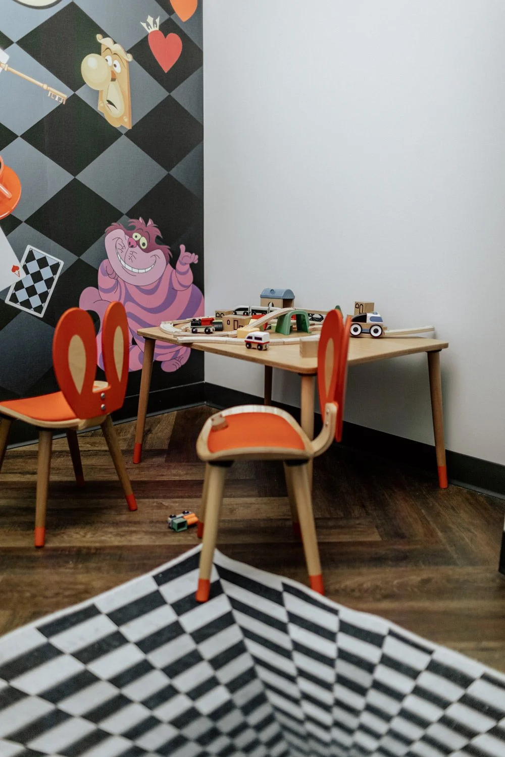 A play area with a wooden table and chairs, toy cars on the table, and a wall decorated with cartoon characters.
