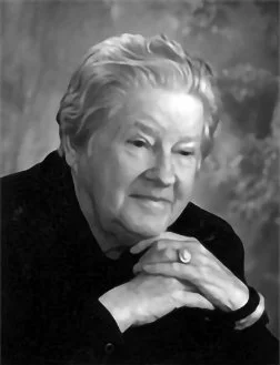 Black and white portrait of an elderly woman with short, wavy hair, resting her chin on her folded hands and looking contemplatively to the side.