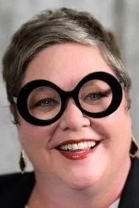 A woman wearing large black glasses and smiling.