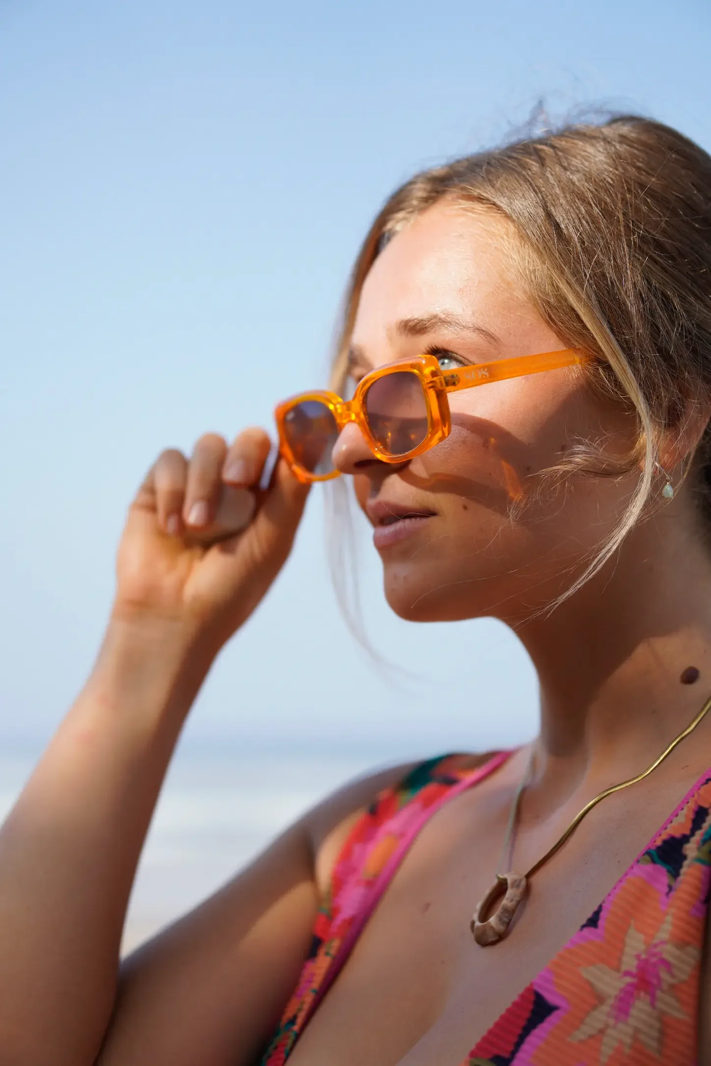 A woman with blonde hair and sunglasses adjusting her glasses on a sunny day.