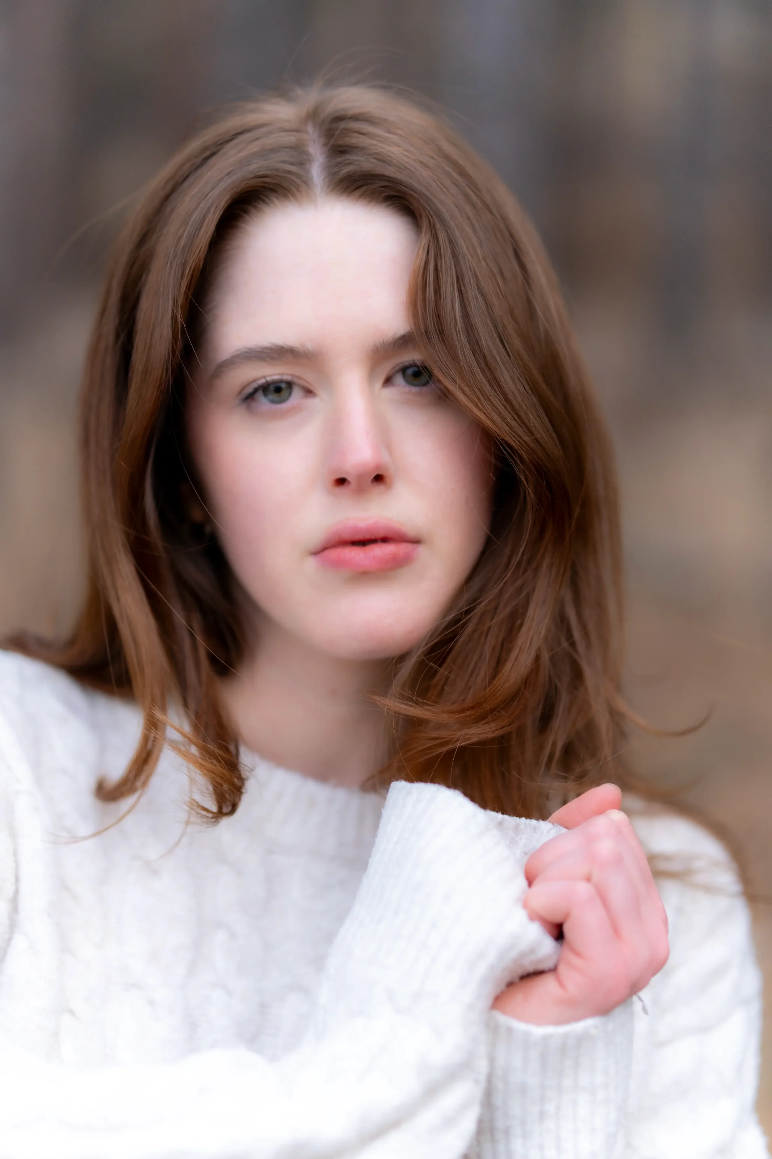 A young woman with red hair and blue eyes wearing a white sweater, making a fist with her right hand.