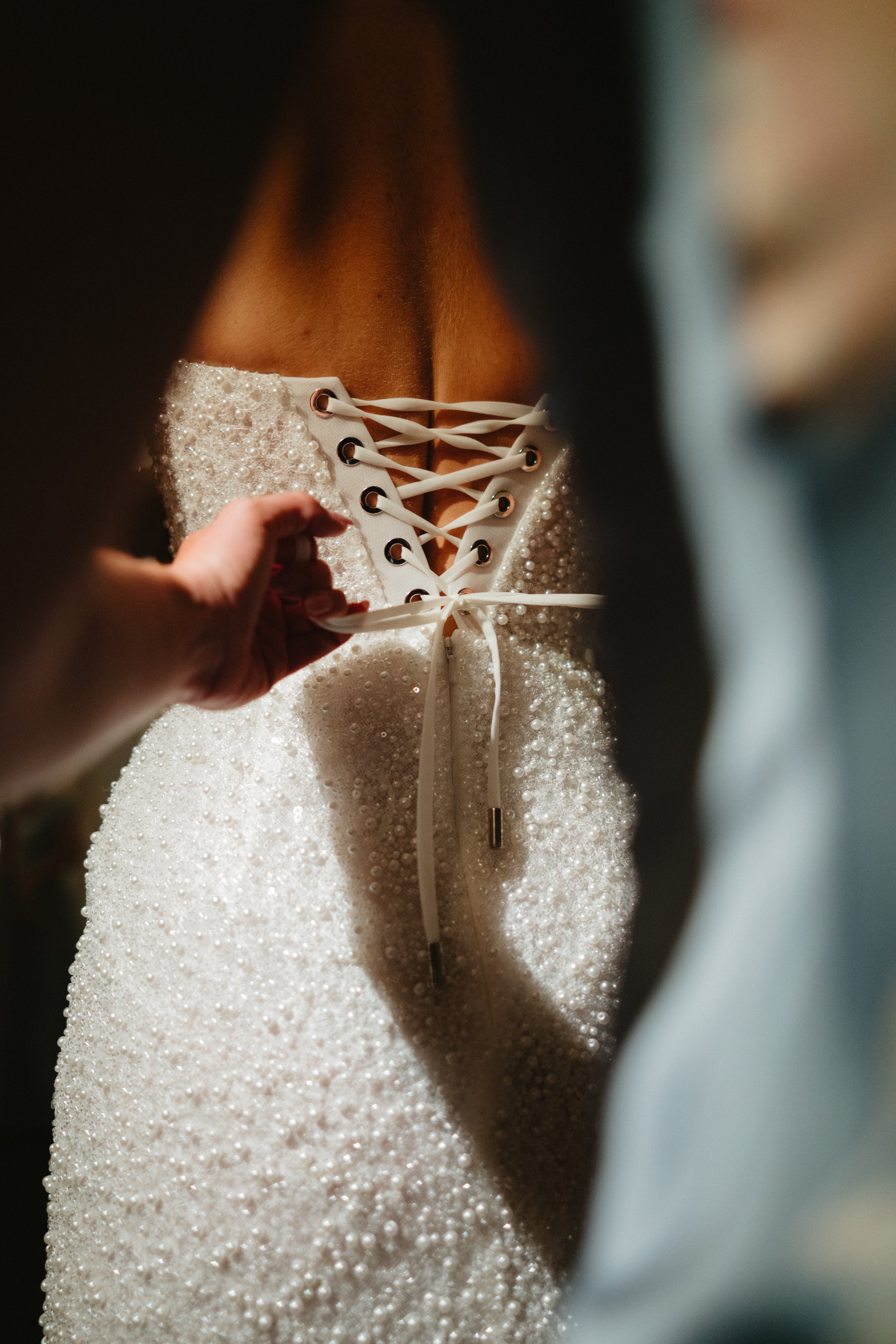 Close-up of a person tying the laces of a white, embellished shoe, with a textured surface covered in small pearls or beads.