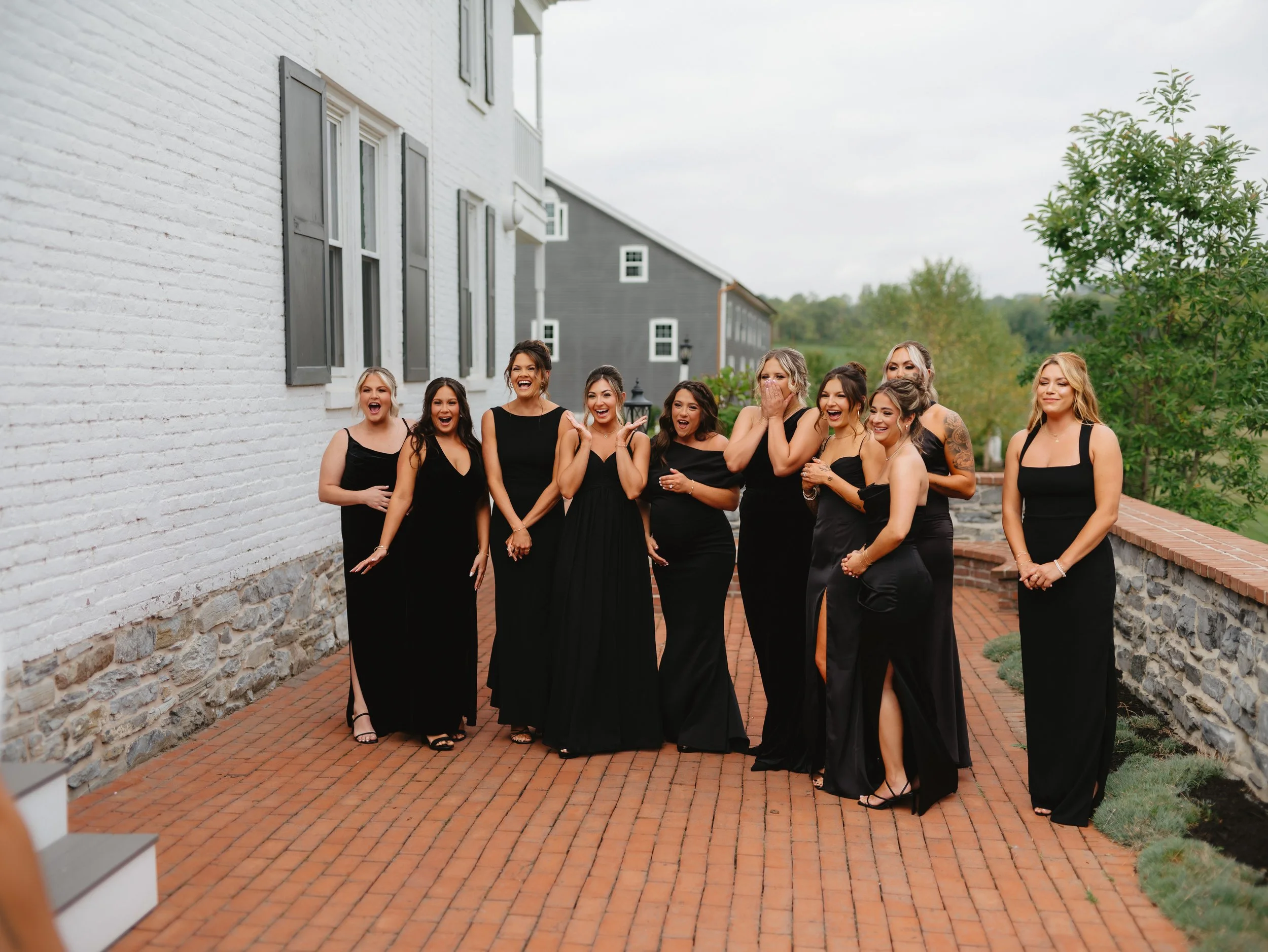 Group of women in black dresses standing on a brick pathway, showing excitement.