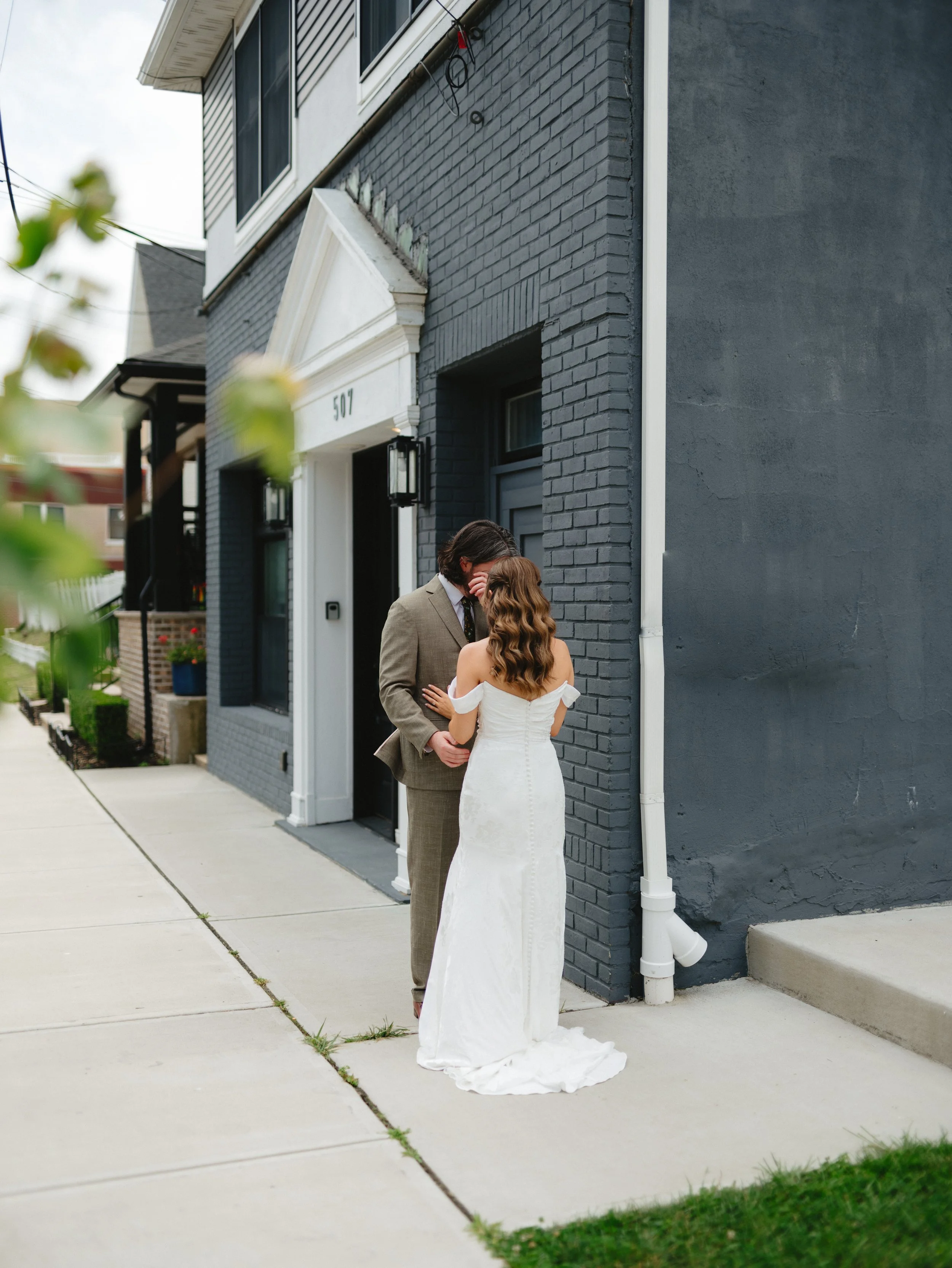 A bride and groom having their first look standing close together outside a modern dark gray building at sunset, sharing an intimate moment in wedding attire. in asbury park new jersey