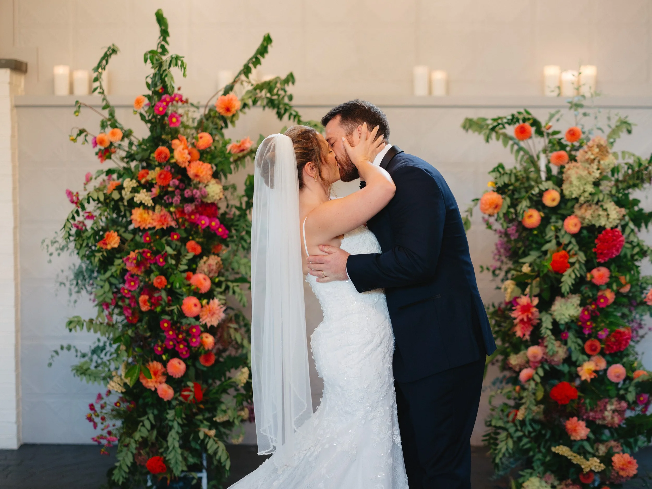 A bride and groom sharing a kiss during their wedding ceremony with floral arrangements in the background.