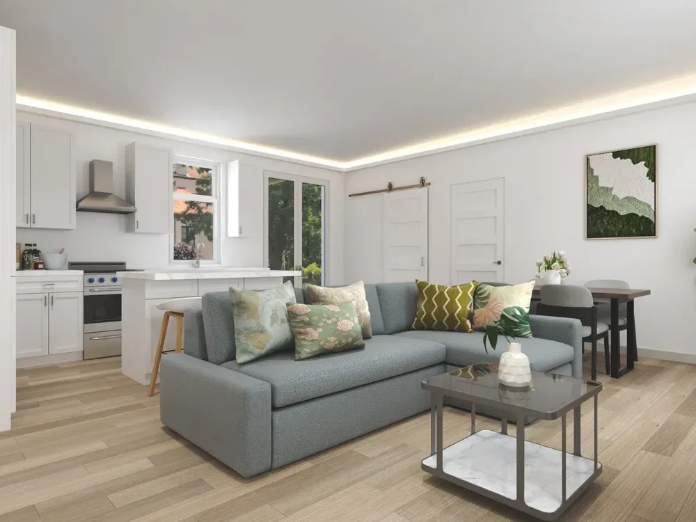 Backyard ADU Modern open-concept living room and kitchen with gray sofa, patterned pillows, coffee table, dining area, and white kitchen cabinets.