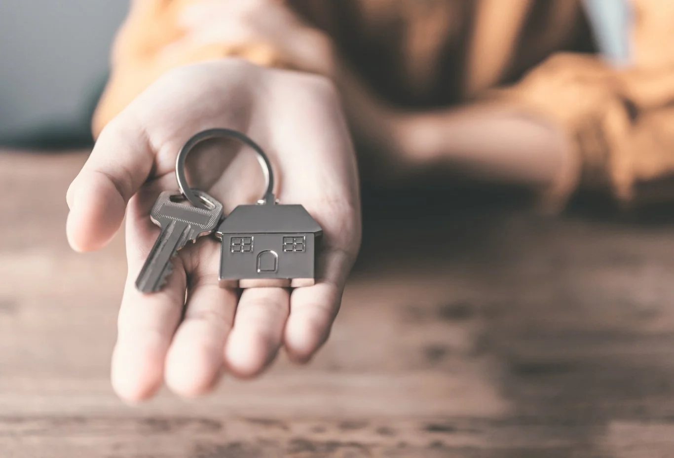 Hand holding a house-shaped keychain with a key for the new ADU homeowner