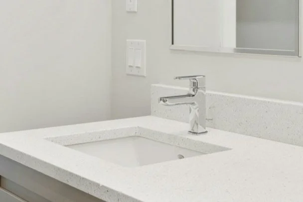 Modern white ADU bathroom sink with a chrome faucet and light switches on the wall.