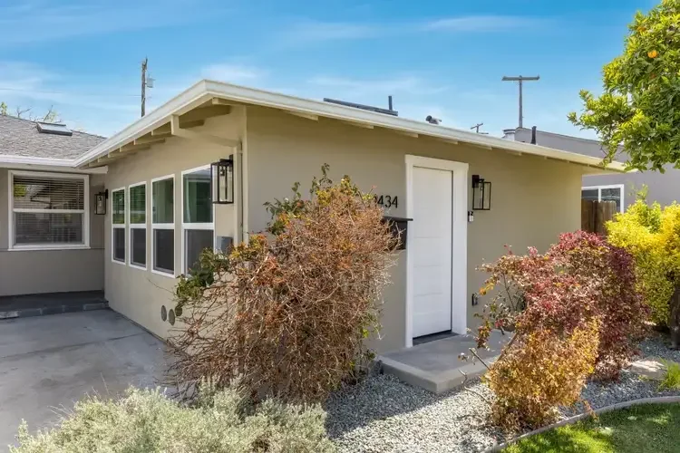 Attached Garage Conversion Studio ADU in front of house with beige exterior, white door, black house numbers, and surrounding shrubs.