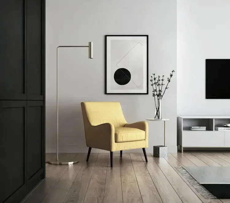 Modern ADU living room with yellow armchair, floor lamp, abstract art, side table with vase, and flat-screen TV.