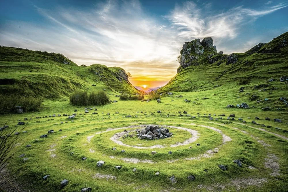 Stones and earth arranged in an ancient circular pattern on a grassy green mountain with the sun setting in the background.