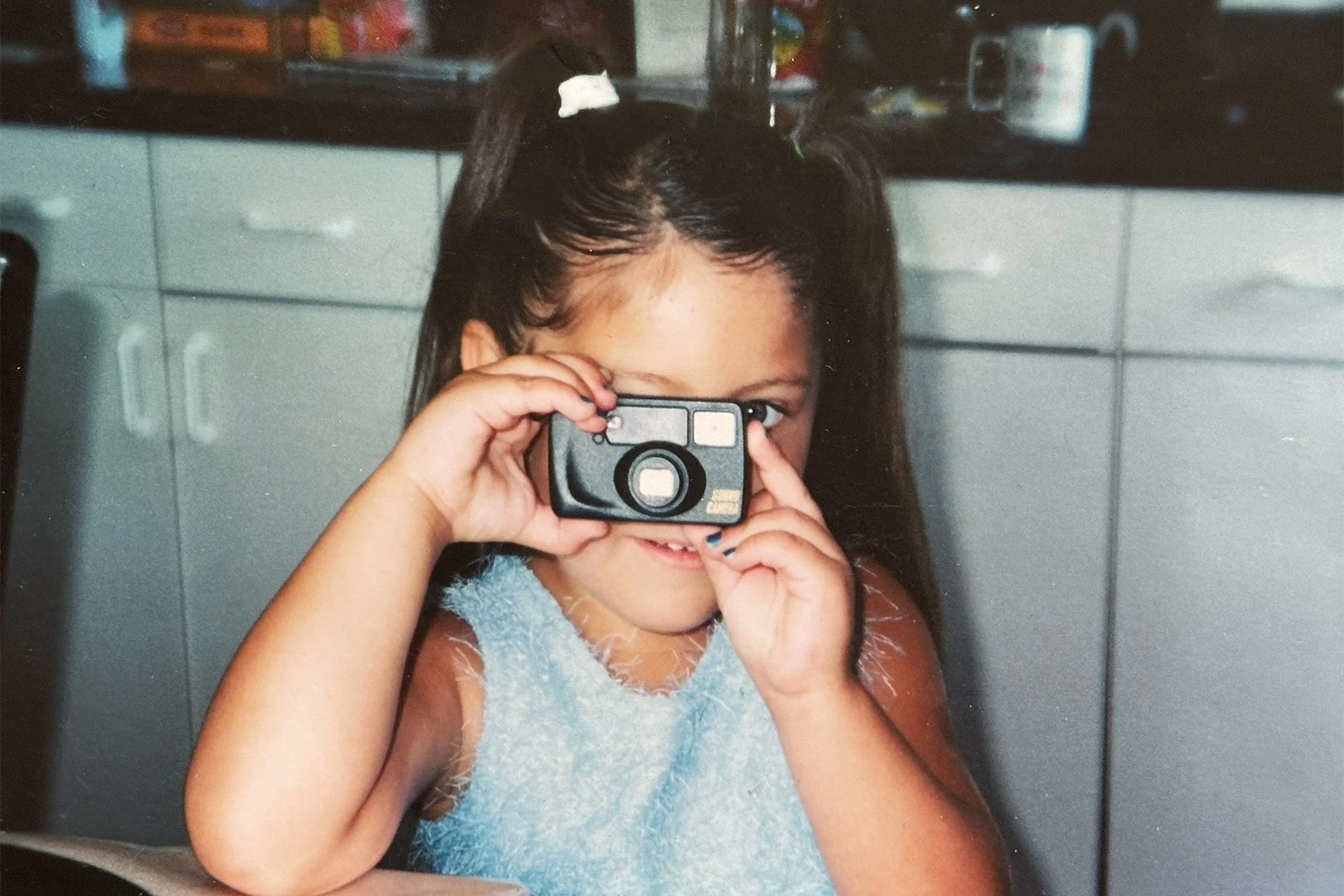 Childhood photo of Lexis holding a toy camera, reflecting the early beginnings of her photography journey.
