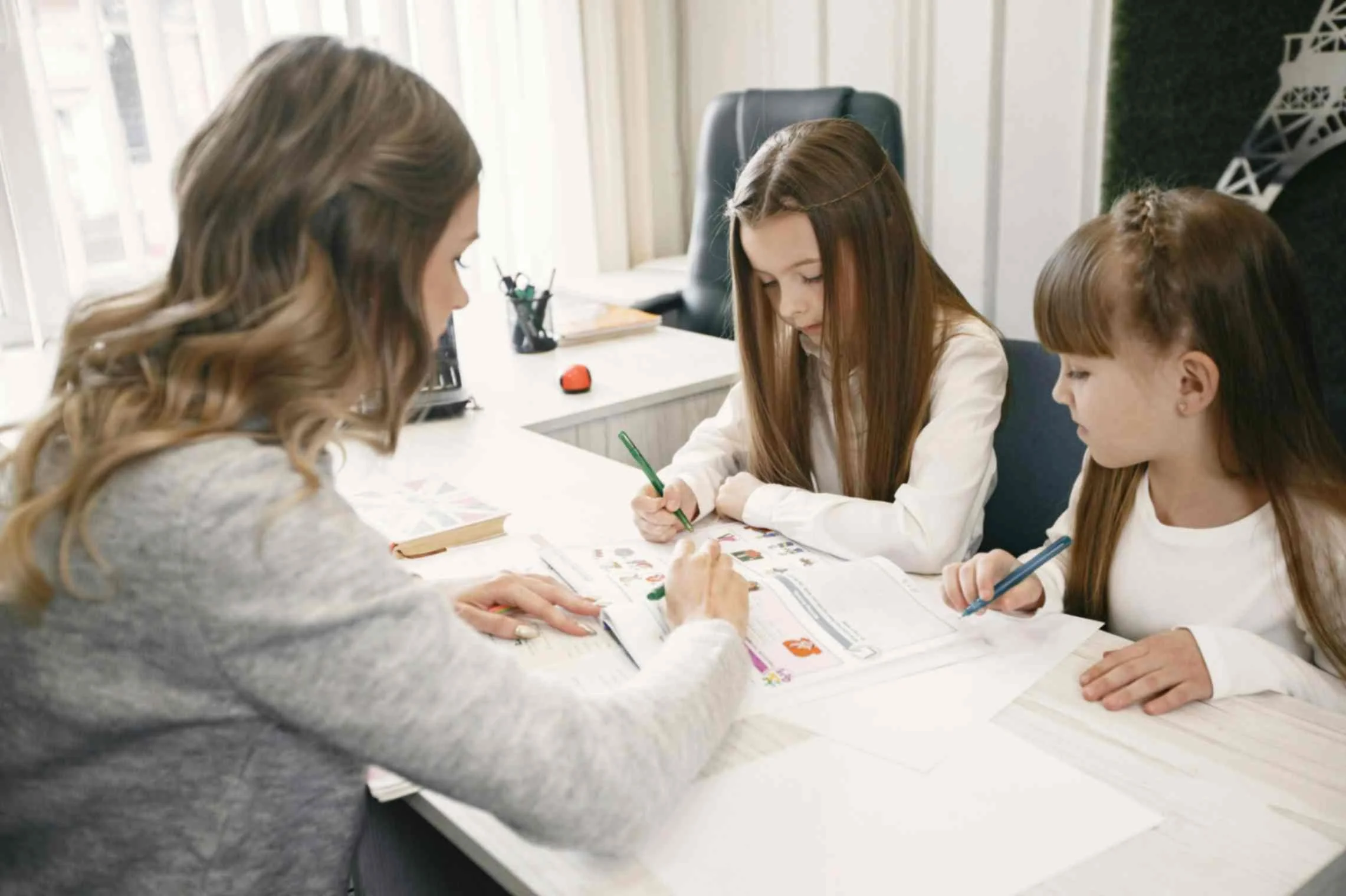 Tutor helping two children study together in a home learning environment