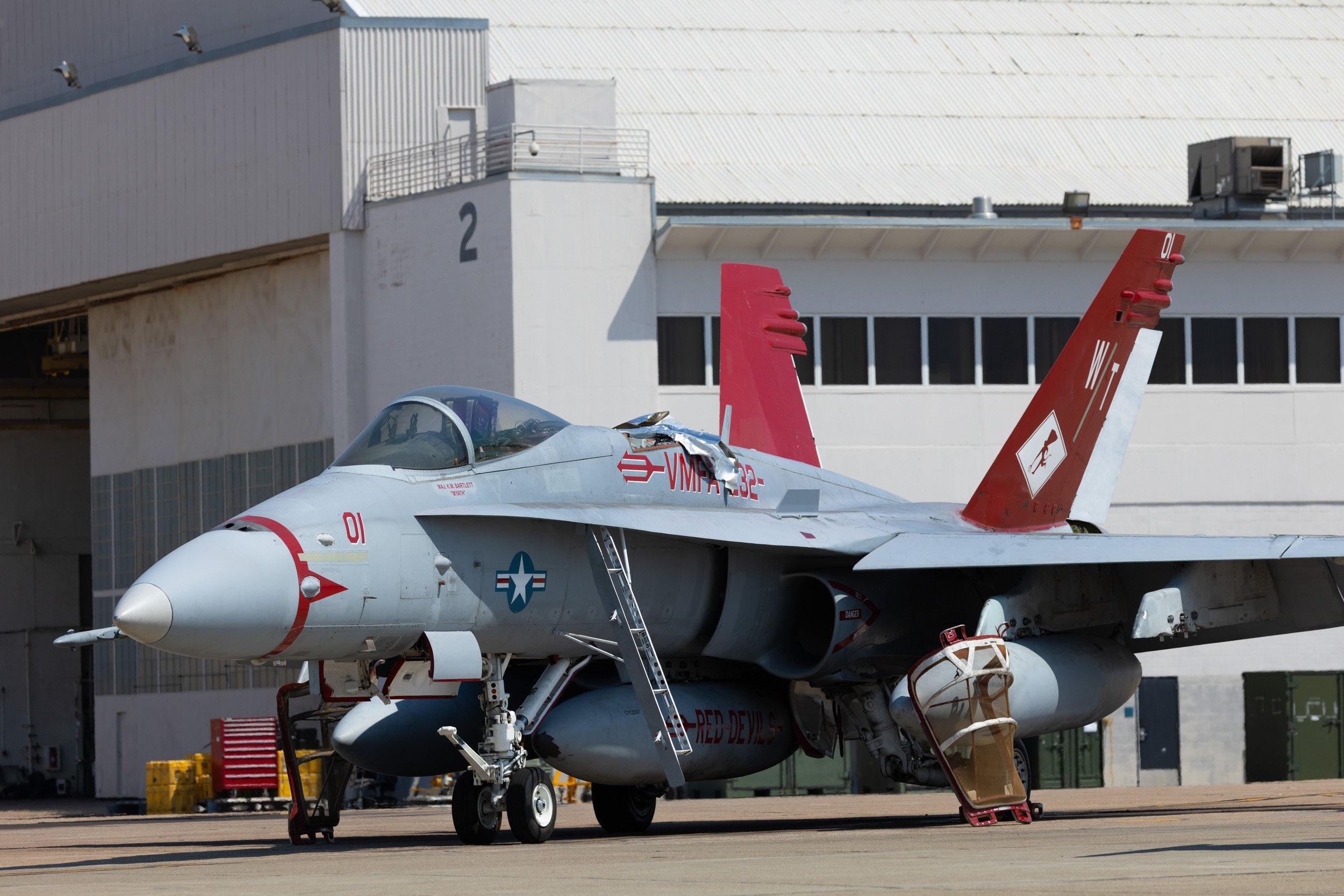 F-16 fighter jet parked on tarmac near hangar with ground equipment.