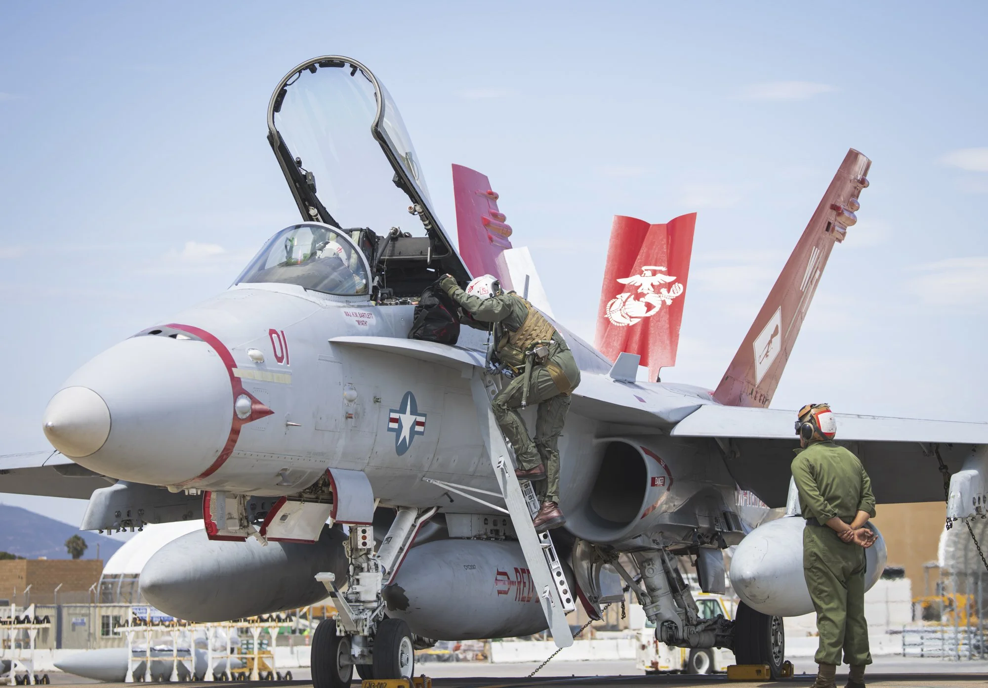 Two pilots preparing a fighter jet for flight; one is entering the cockpit, the other is standing nearby on the tarmac, with a clear sky background.