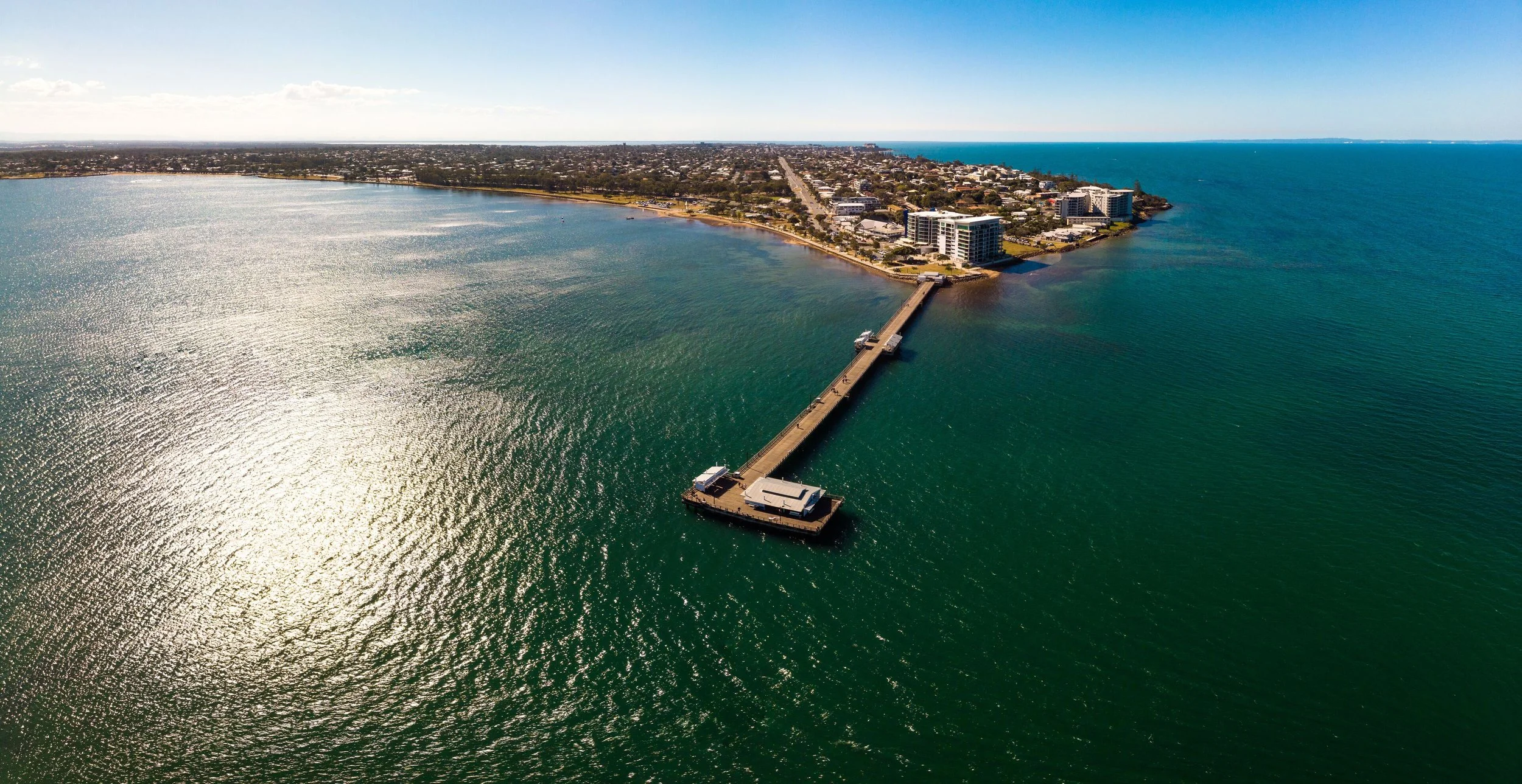 An aerial view of a pier extending into a large body of water with a city in the background. Woody Point