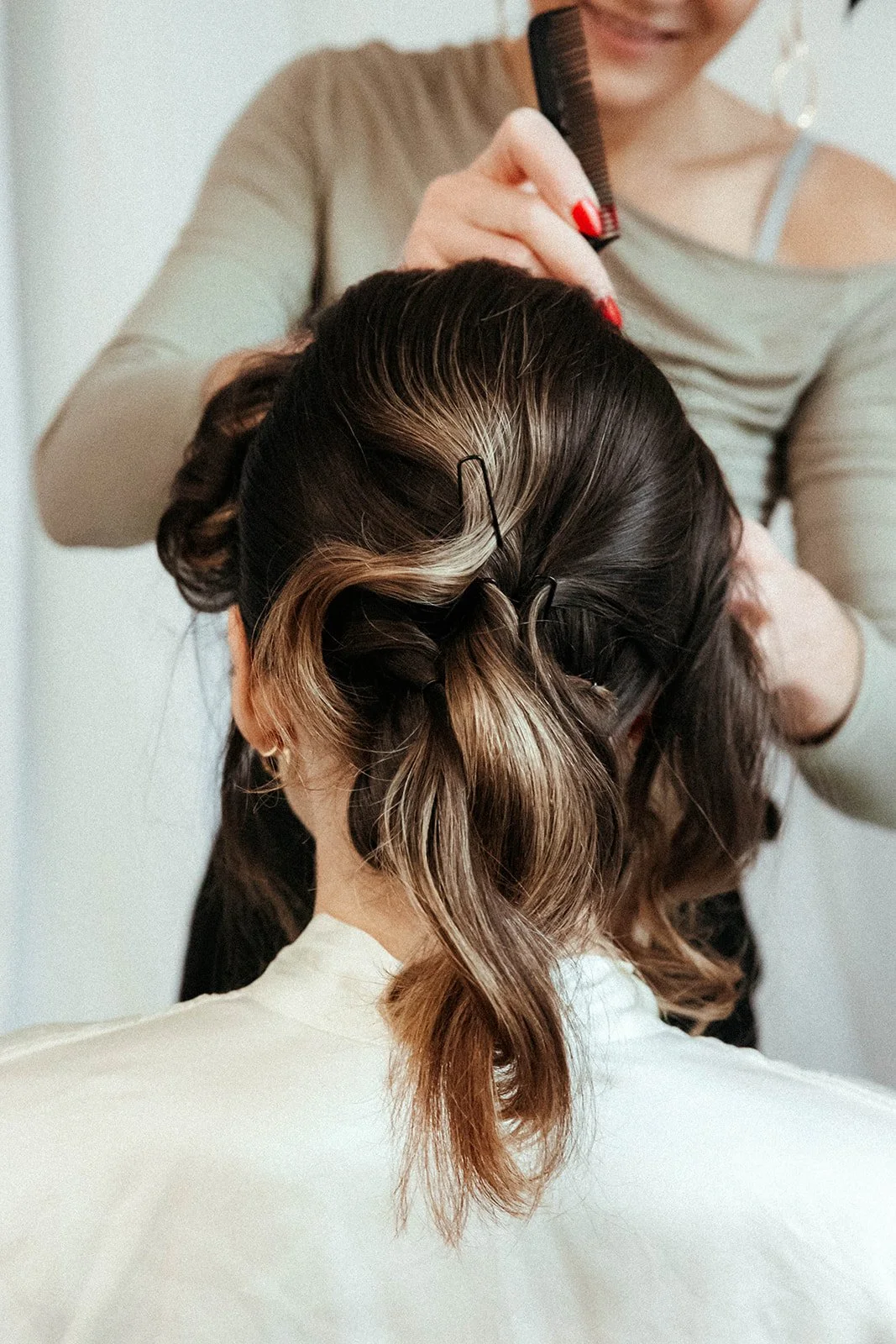 Friseurin stylt eine Frau mit braunem Haar, das teilweise blond gefärbt ist, unter Verwendung von Haarklammern.