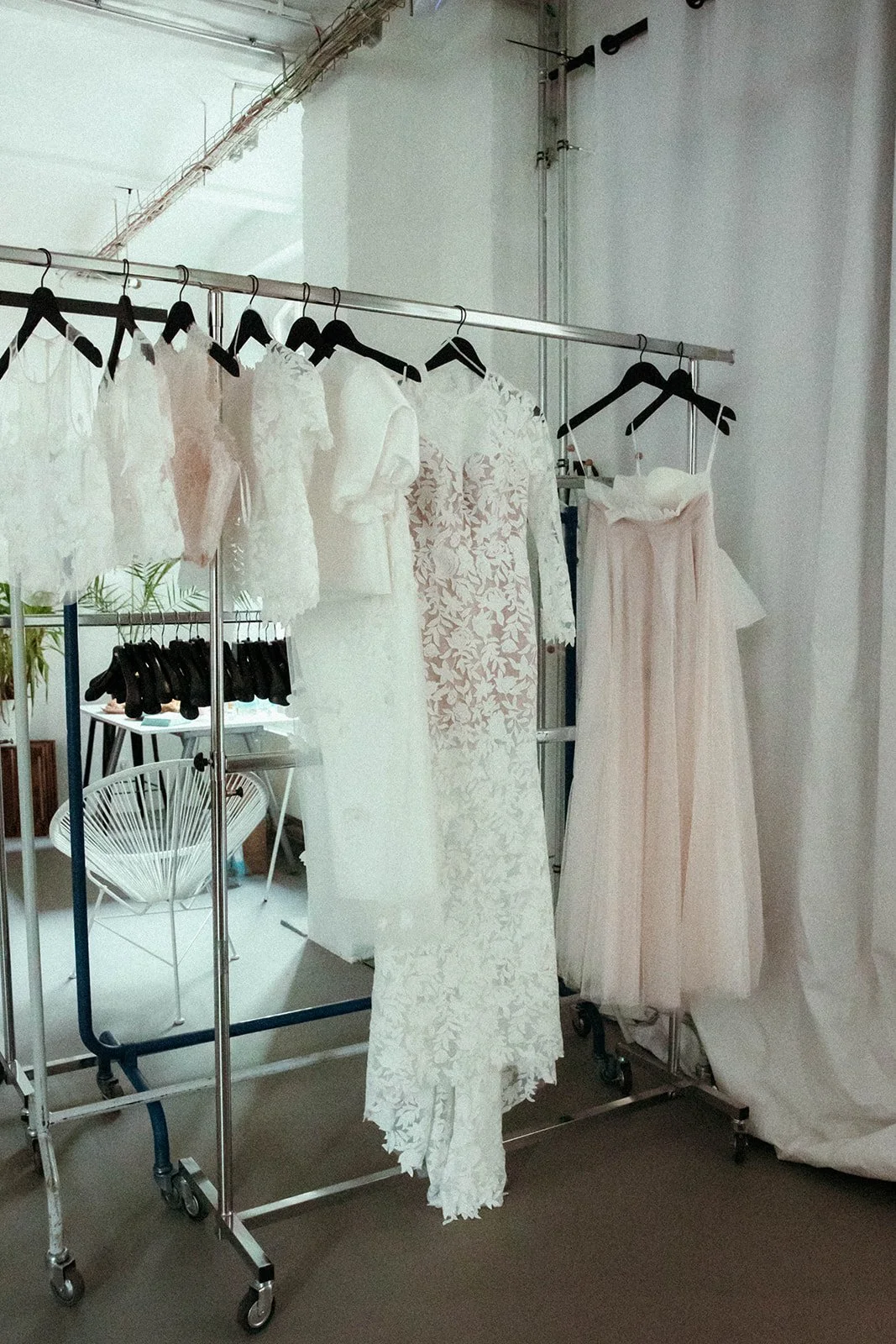 Kleiderstange mit weißen Brautkleidern und Haarschleifen, im Hintergrund weiße Wände und eine weiße Fraschstuhl.