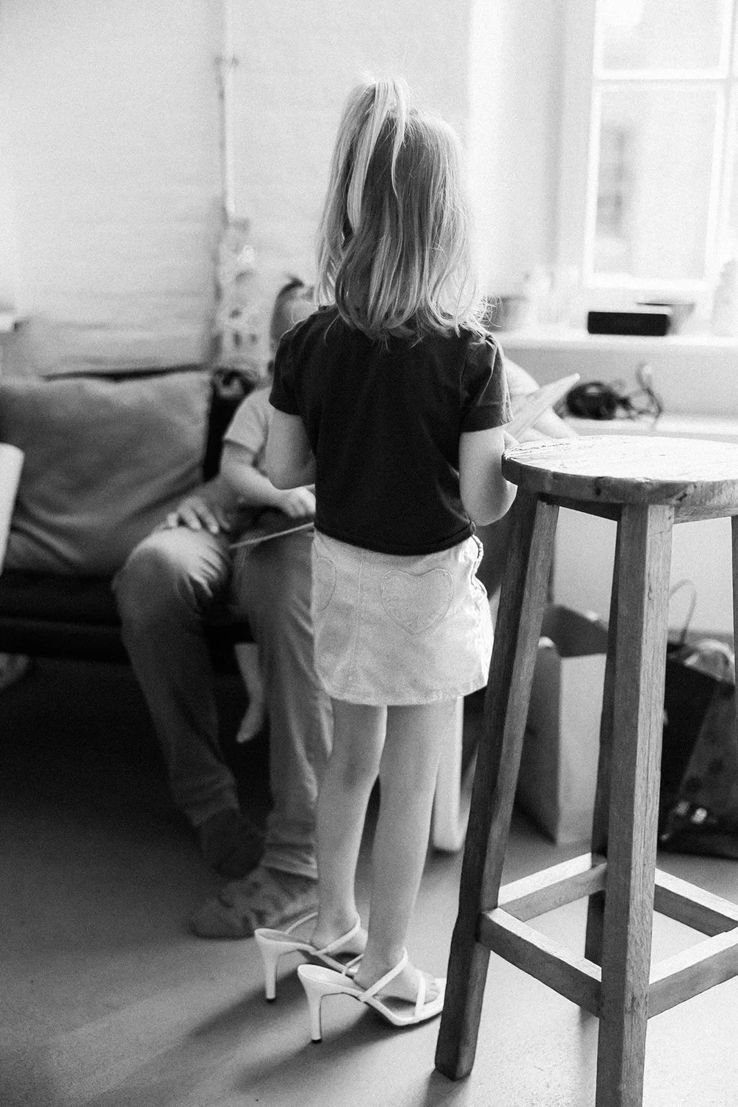 Ein Mädchen trägt High Heels beim Spielen in einem Wohnzimmer mit einer Sitzecke und einem Tisch.