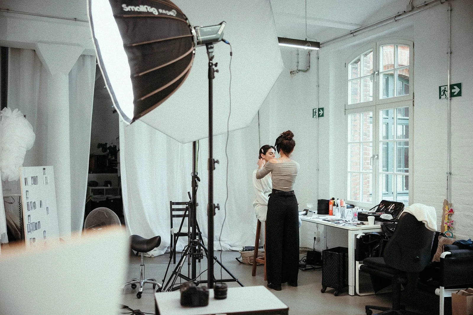 Fotostudio mit zwei Frauen bei Make-up, professionelle Beleuchtung, Whiteboard, Fenster, neues und kreatives Arbeitsumfeld.