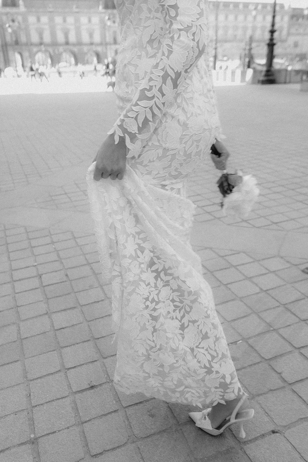Frau in einem hochzeitskleid läuft auf Kopfsteinpflaster, hält einen Blumenstrauß in der Hand.