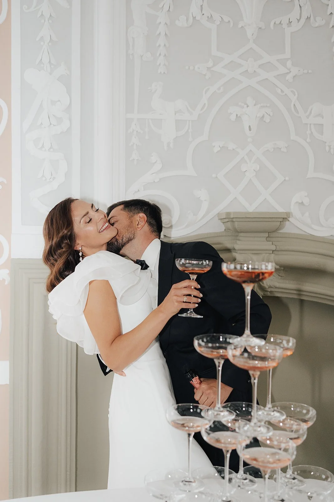 Ein glückliches Brautpaar beim Kuss während einer Hochzeit, umgeben von Sektgläsern