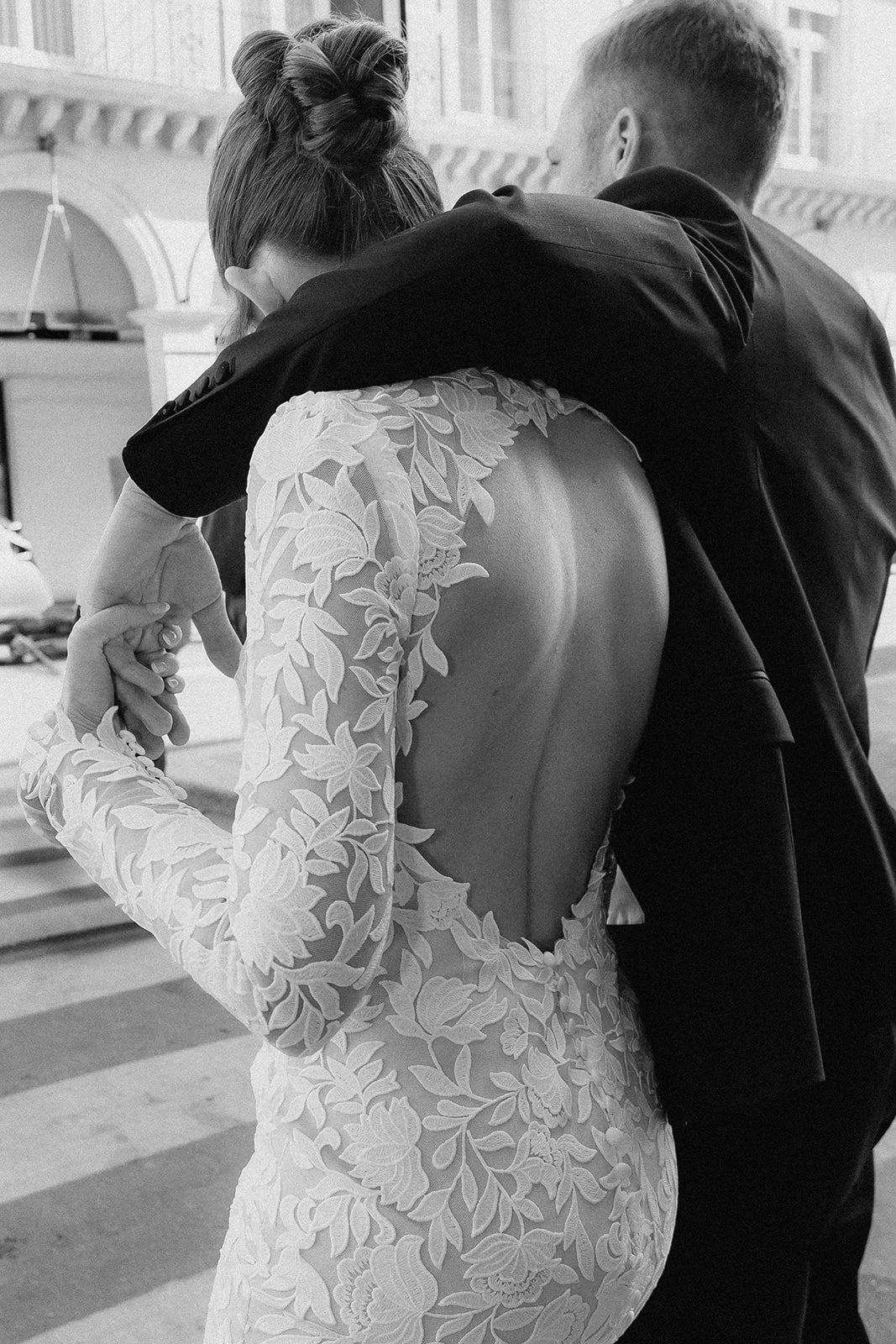 Braut in einem eleganten, mit Blumenmuster verzierten Kleid mit offenem Rücken, die von einem Mann getröstet wird.