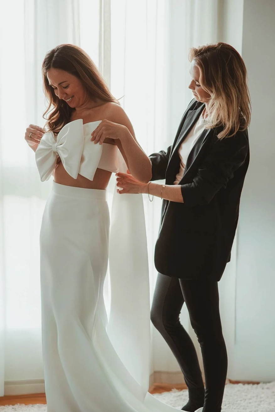 Einer Braut wird von der Designerin bei der Anprobe ihres Hochzeitskleides geholfen.