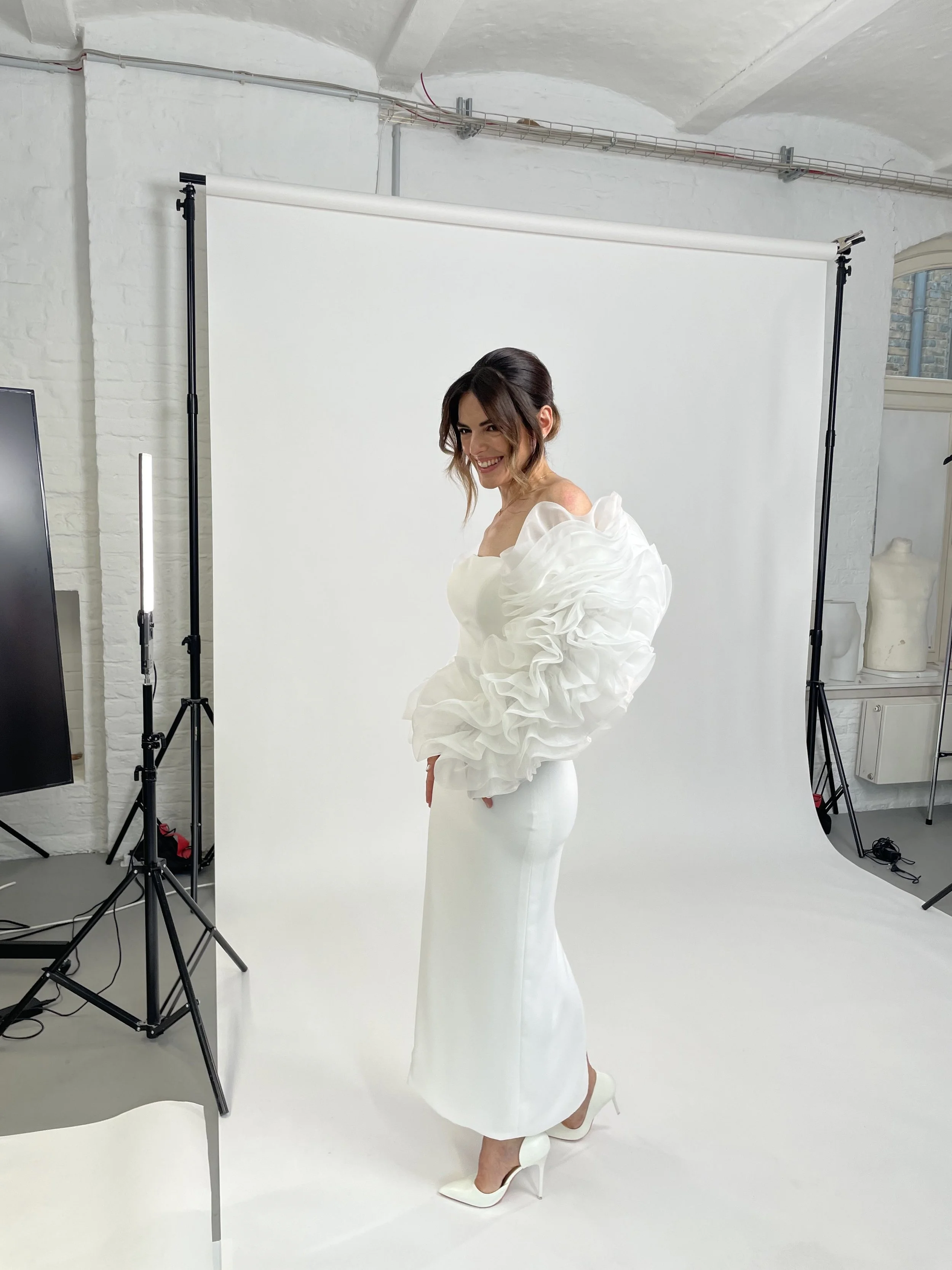 Frau trägt ein elegantes weißes Brautkleid mit großen, rüschigen Puffärmeln, in einem Fotostudio vor weißem Hintergrund.
