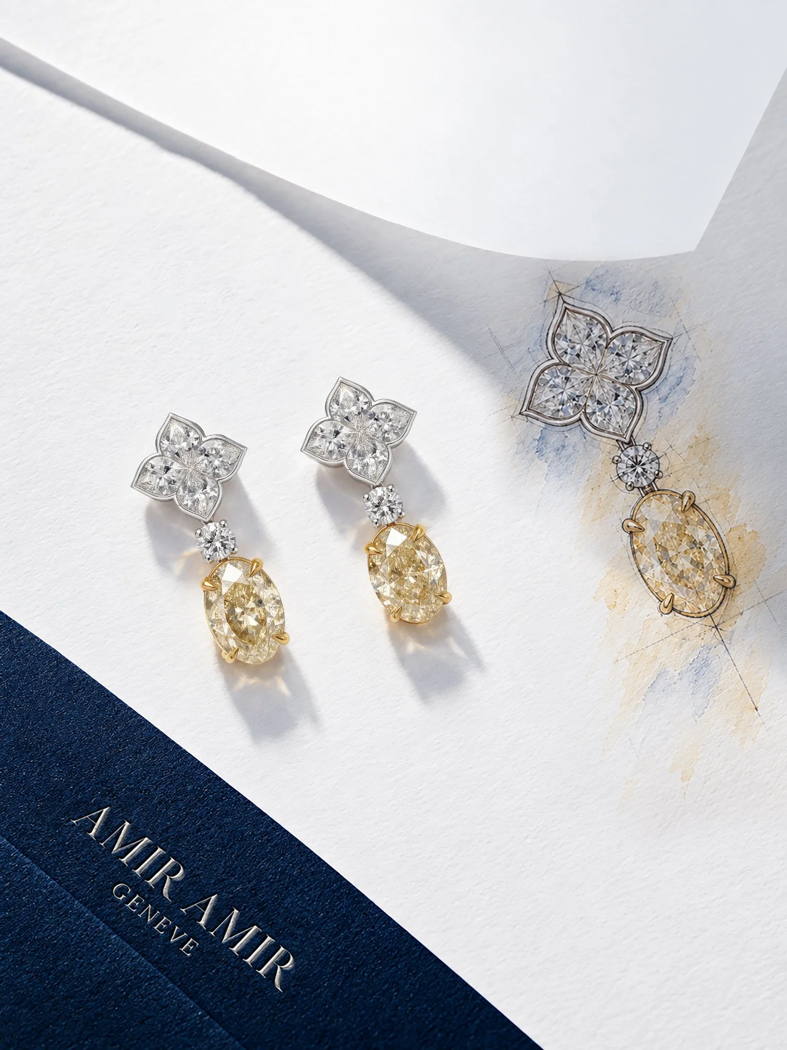 AMIRAMIR LILY diamond drop earrings arranged on white fabric beside a jewellery design sketch, featuring floral diamond tops and yellow oval drops.