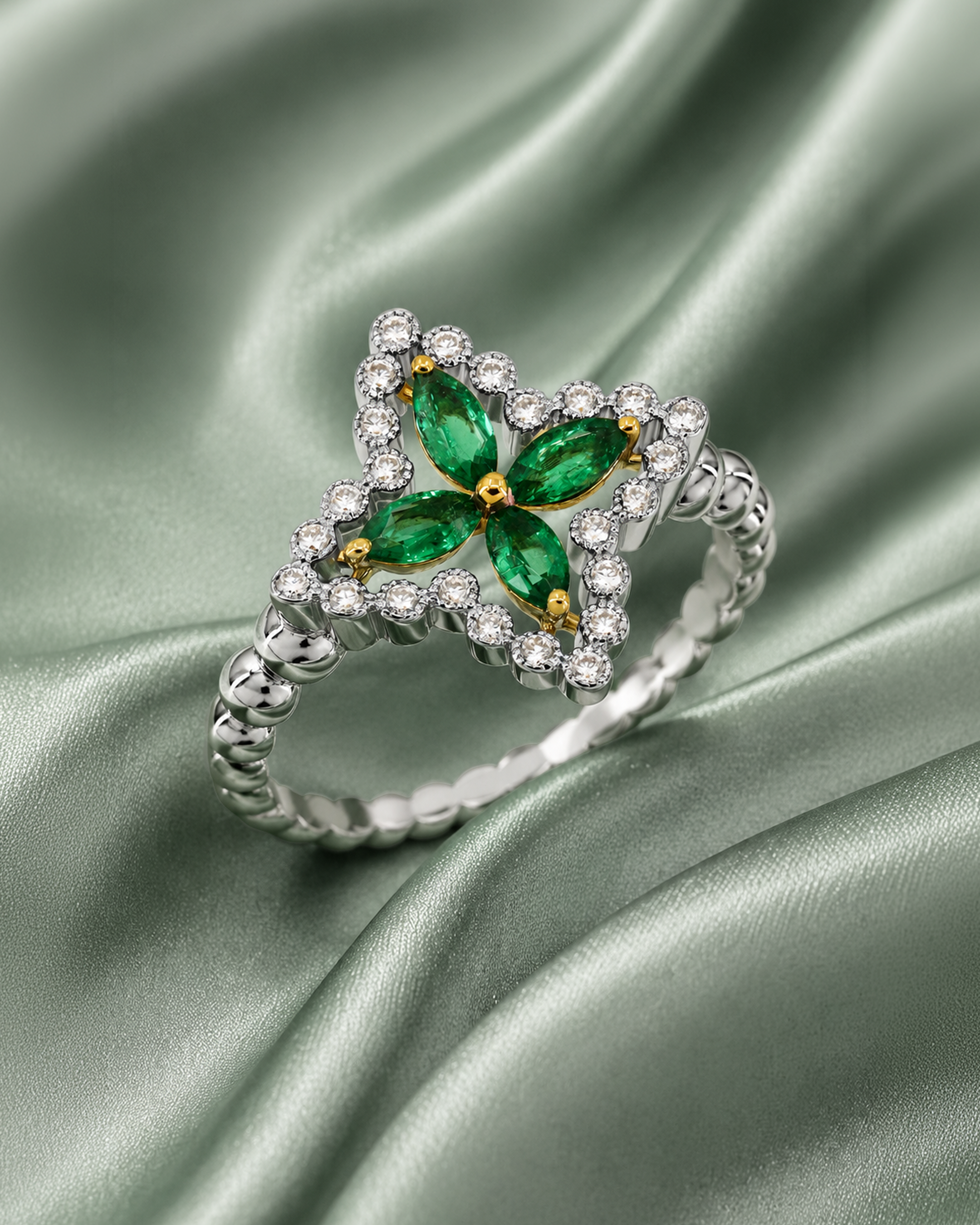 Silver ring with green gemstone and surrounding small diamonds, placed on green satin fabric.