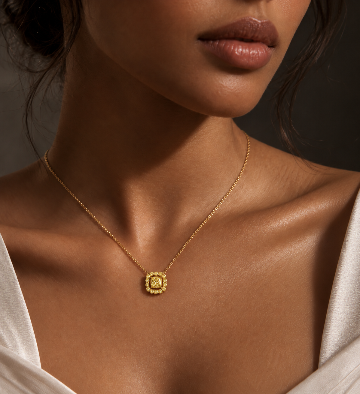 AIR Cushion Fancy Yellow Diamond Pendant worn on the neck, with a fancy yellow cushion-cut center diamond surrounded by fancy yellow round diamonds in 18K yellow gold.