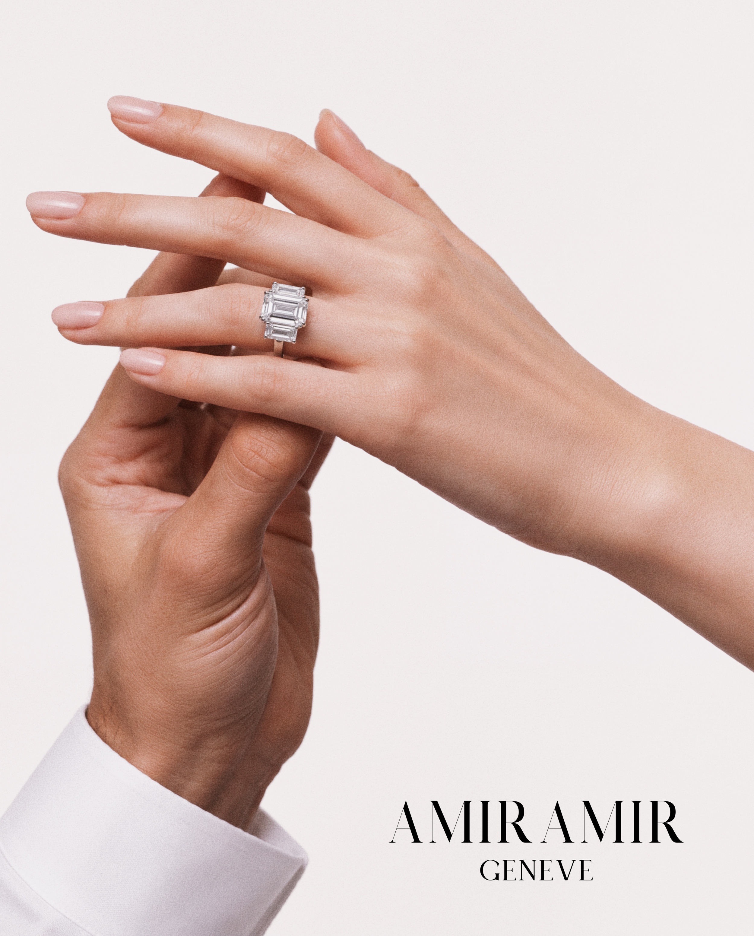 Close-up of a couple’s hands showcasing the AMIRAMIR FOREVER three-stone emerald-cut diamond engagement ring, with the AMIRAMIR Genève logo.