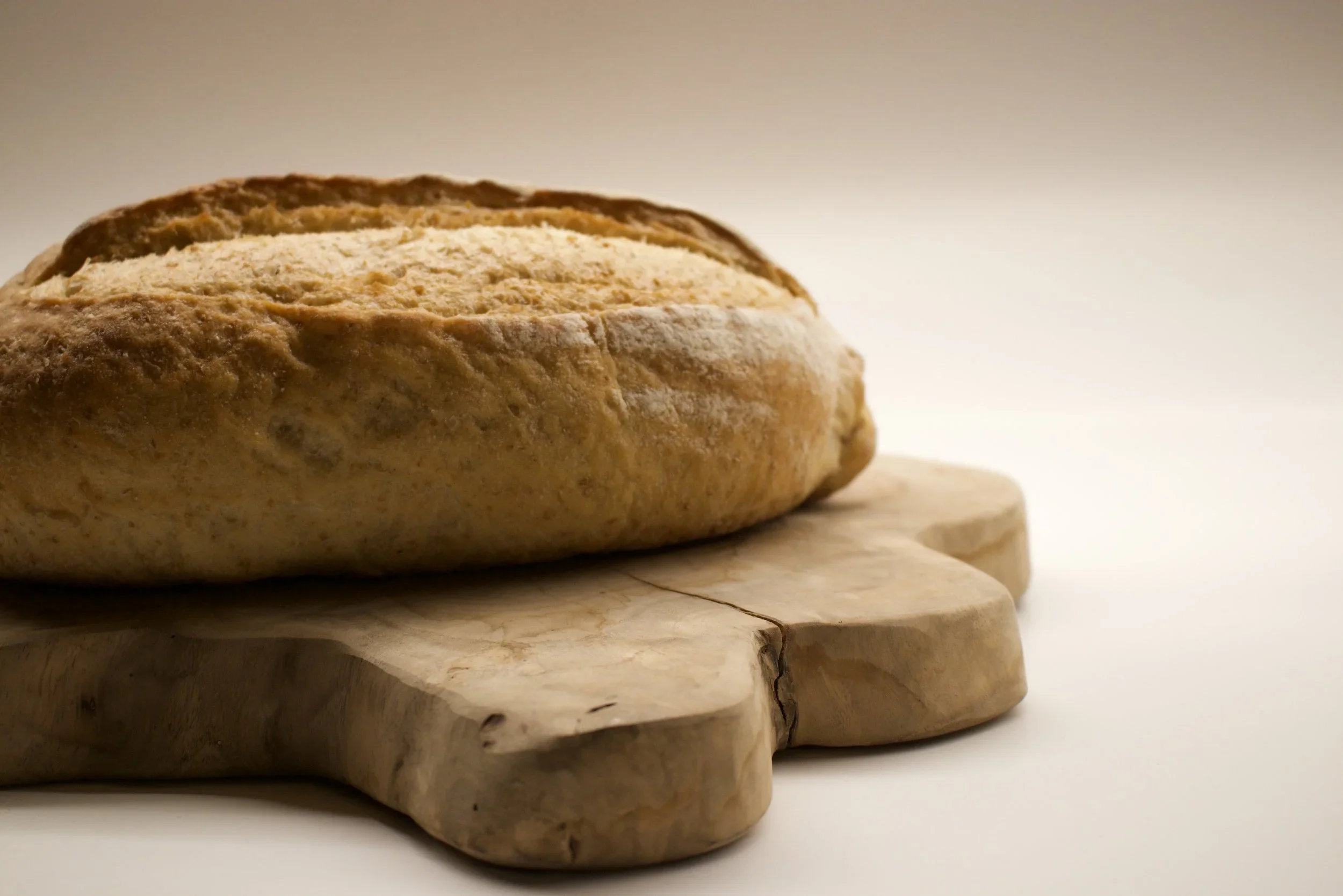 A loaf of bread with a golden crust on a wooden cutting board against a plain background.