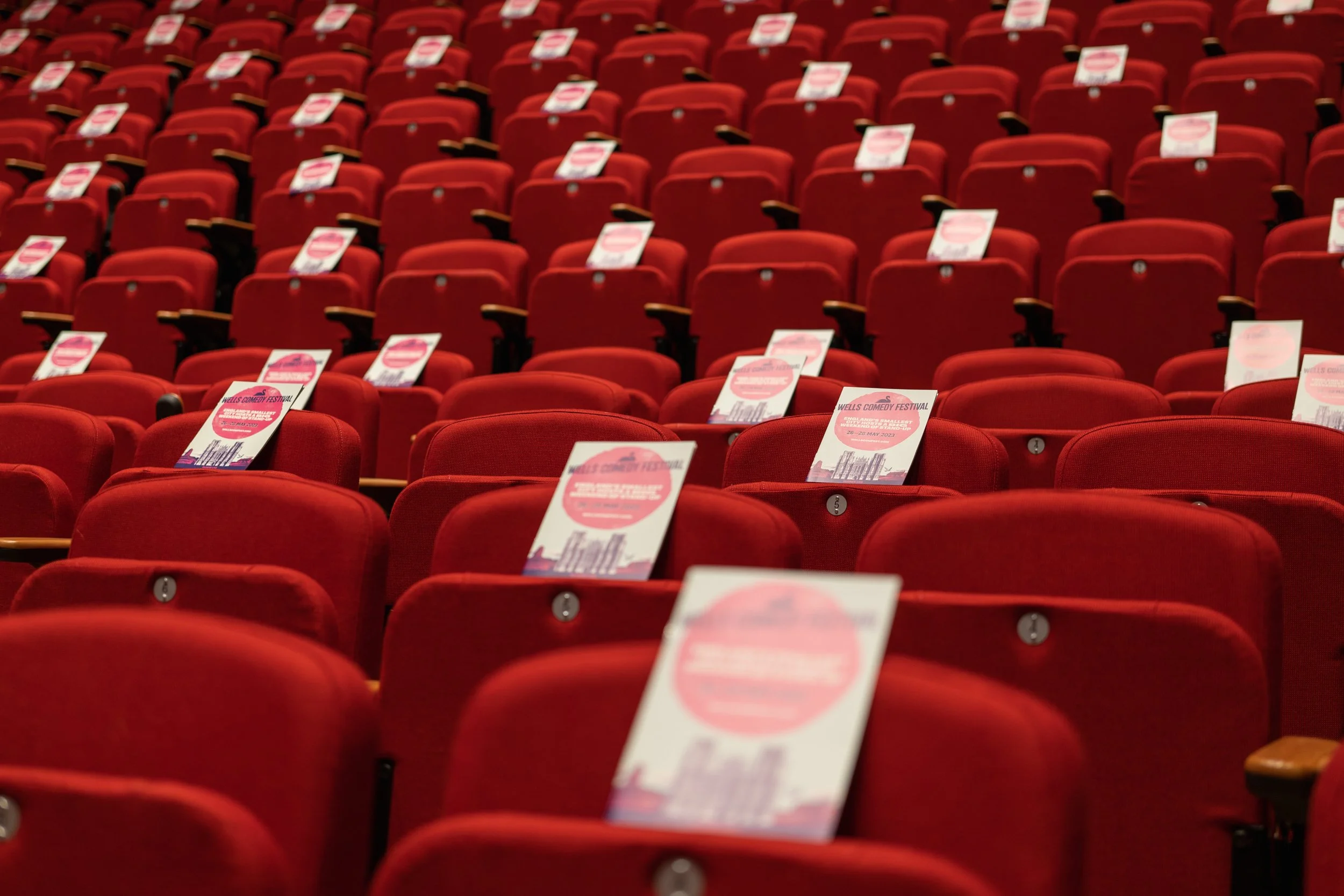 Rows of red theater seats with event flyers placed on each seat.
