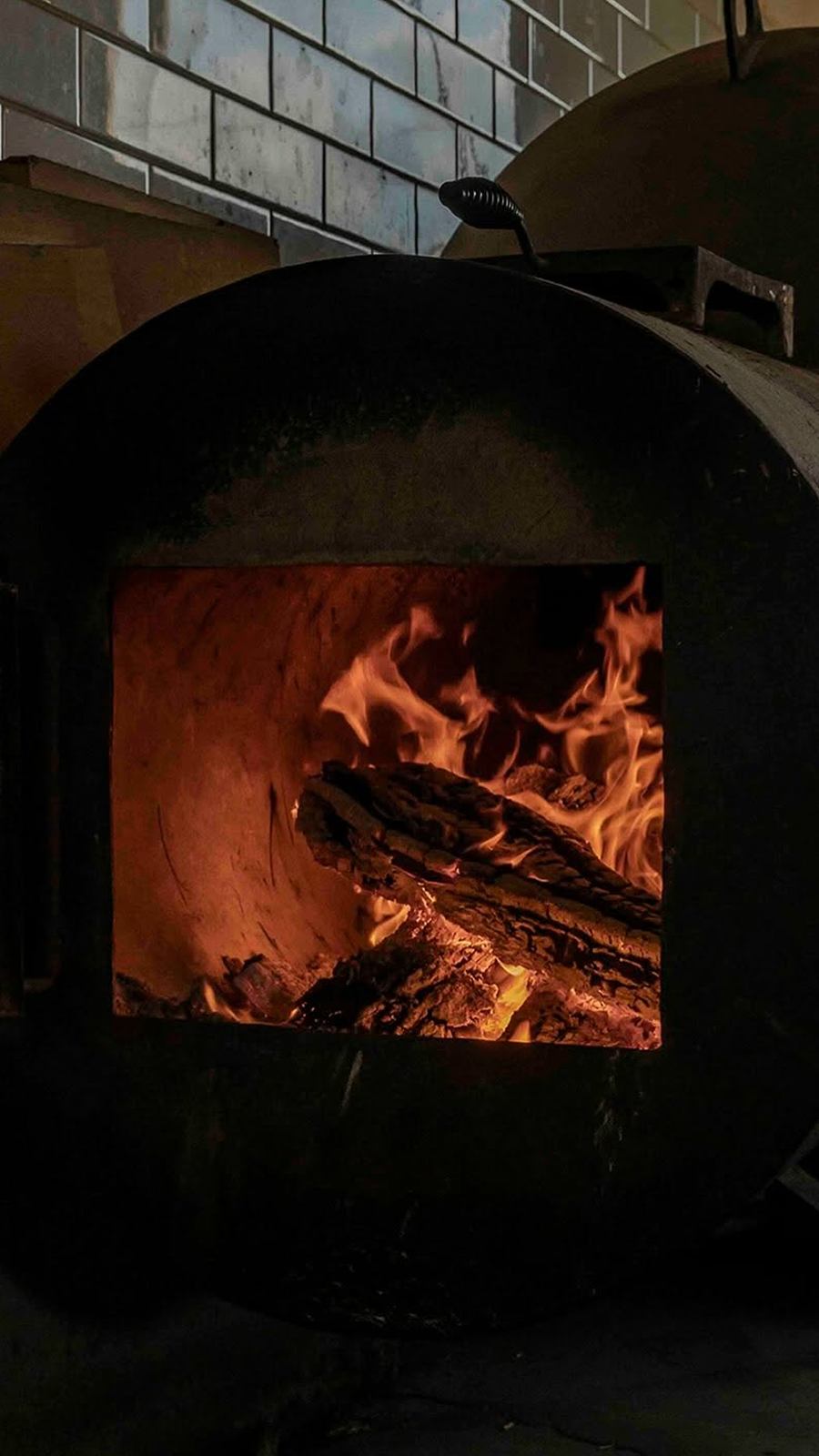 A close-up of a wood-fired oven with flames and burning wood inside.