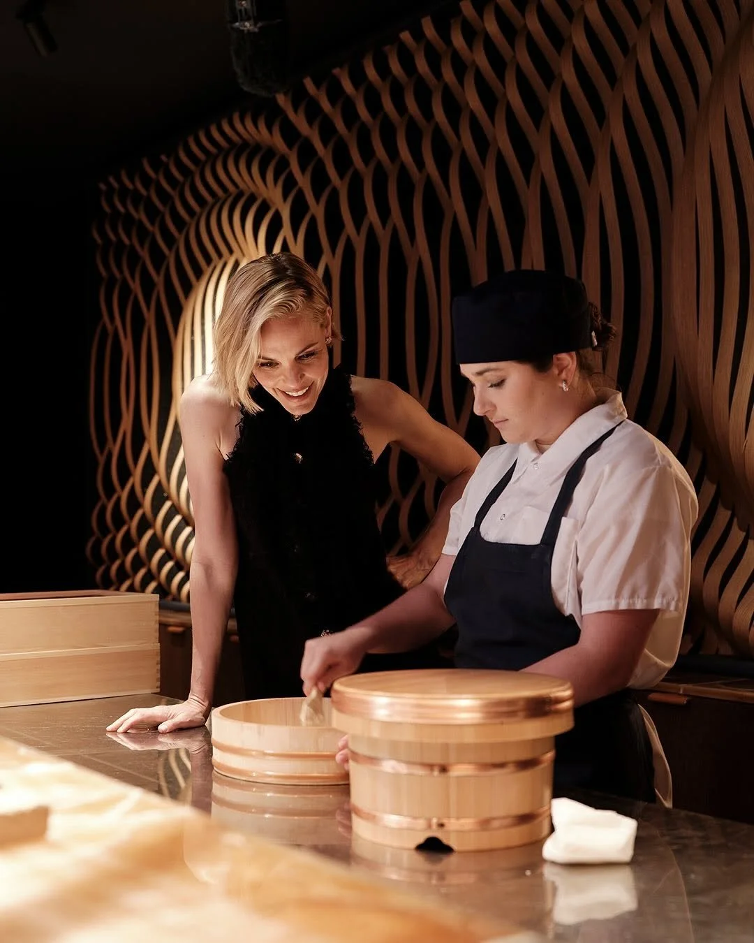 A woman and a chef in a restaurant kitchen, preparing food with wooden steamers.