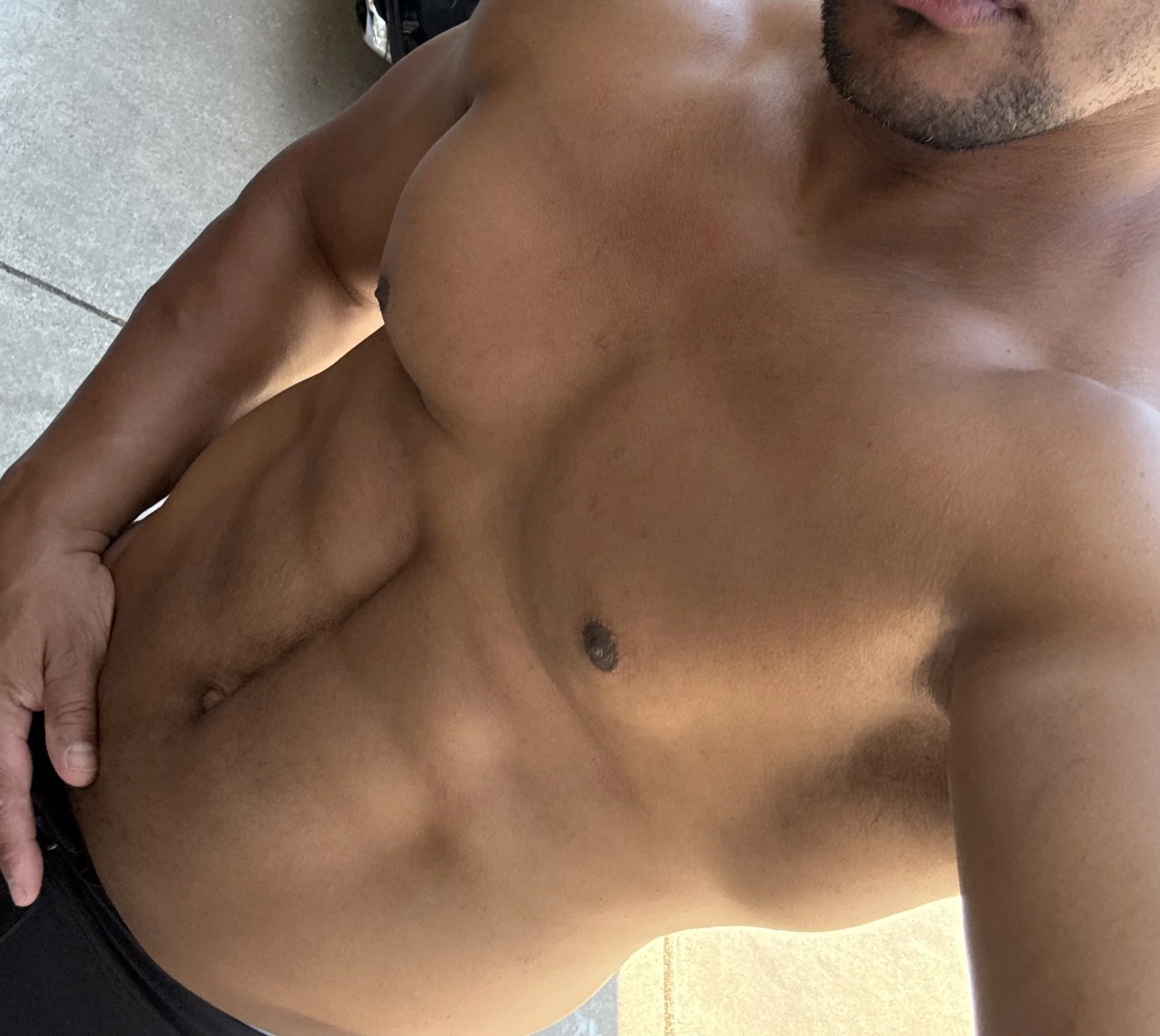 A shirtless man with tanned skin taking a selfie, showing his chest and abdomen, with his head partially out of the frame.