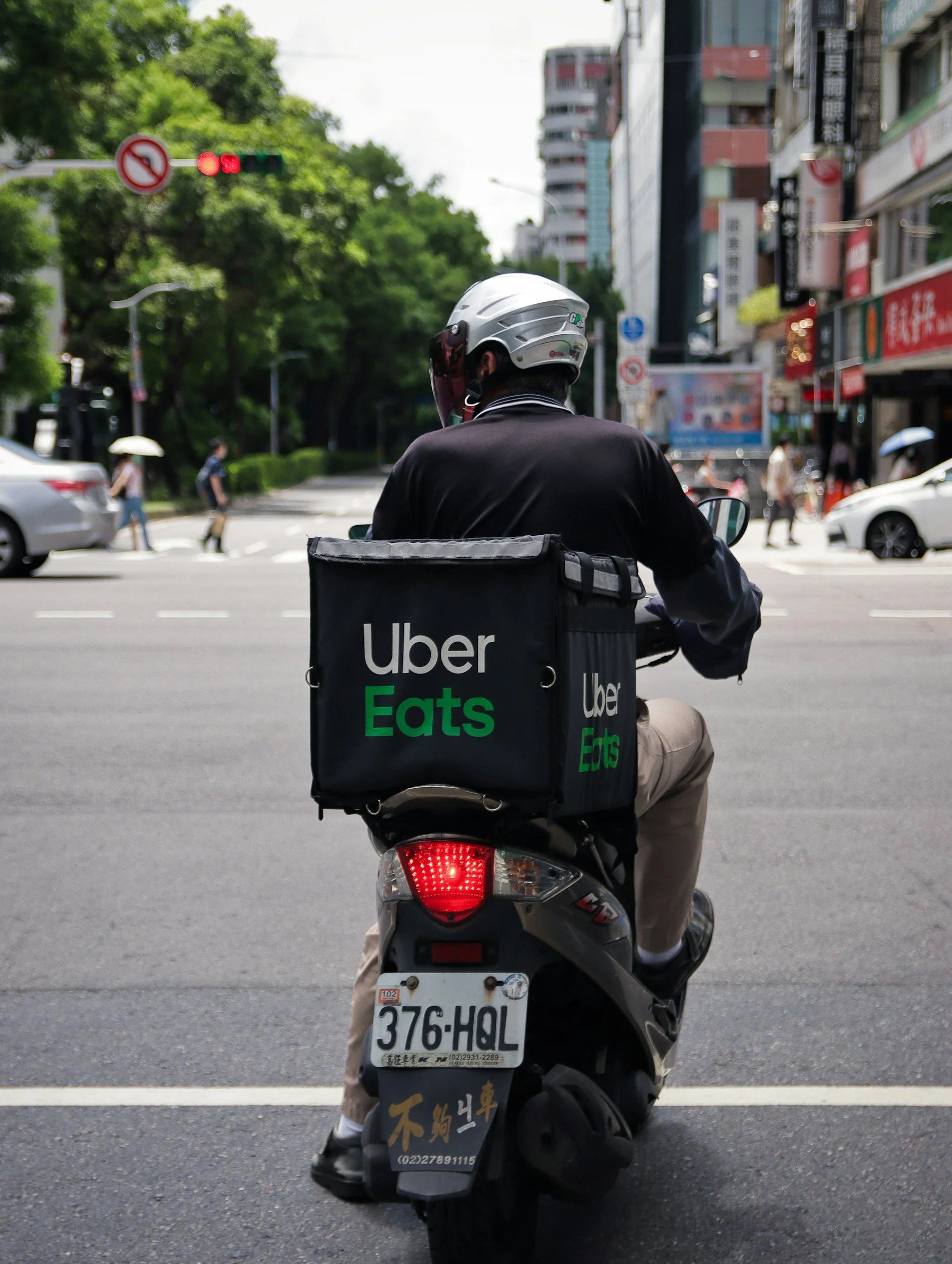 Uber Eats delivery person on a scooter waiting at an intersection in a city.