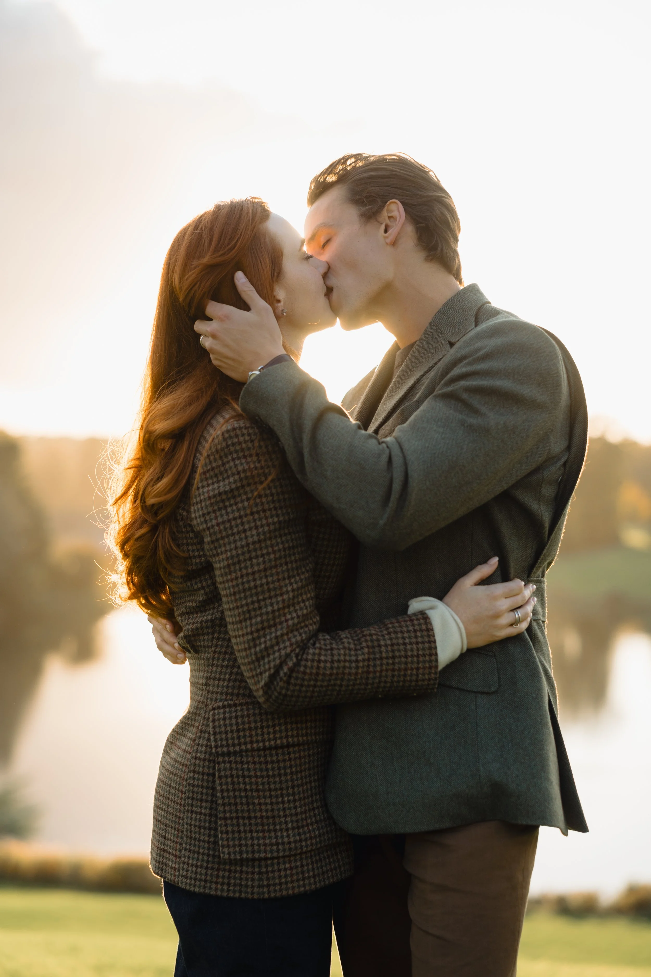 A man and woman sharing a kiss outdoors during sunset, embracing each other affectionately.