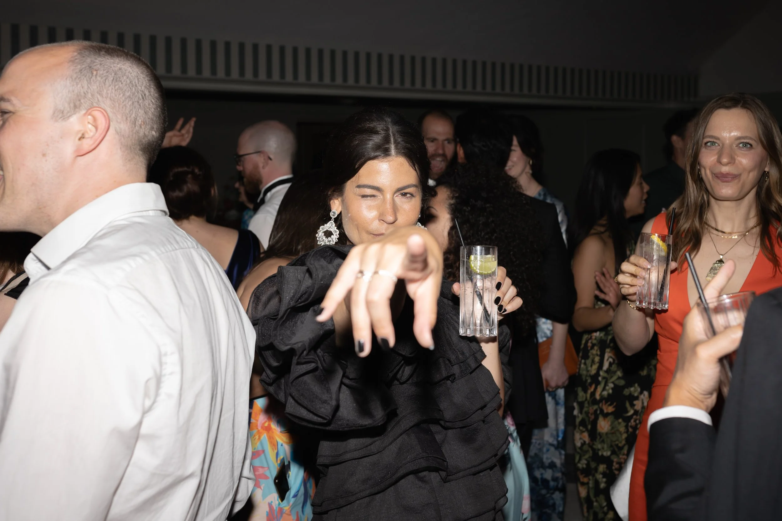 People enjoying a party with drinks, women in dresses and men in suits, celebrating in a lively indoor setting.