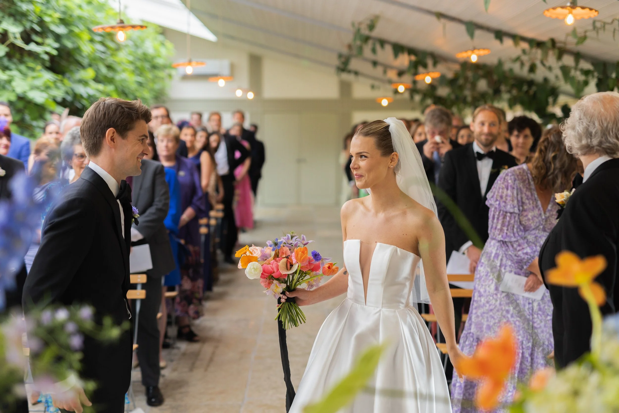 Bride and groom facing each other during their wedding ceremony, surrounded by guests in a decorated venue.