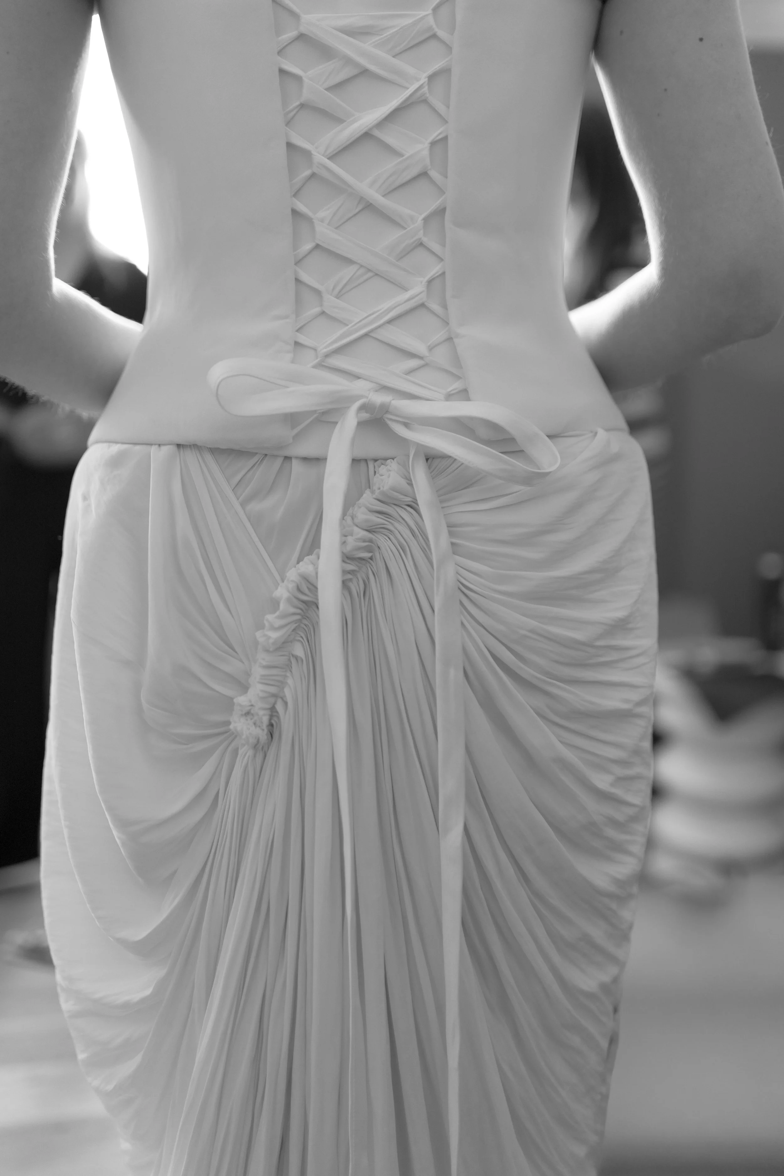 Close-up of a woman wearing a backless, lace-up wedding dress with a ruched skirt from Angeline Brunk.