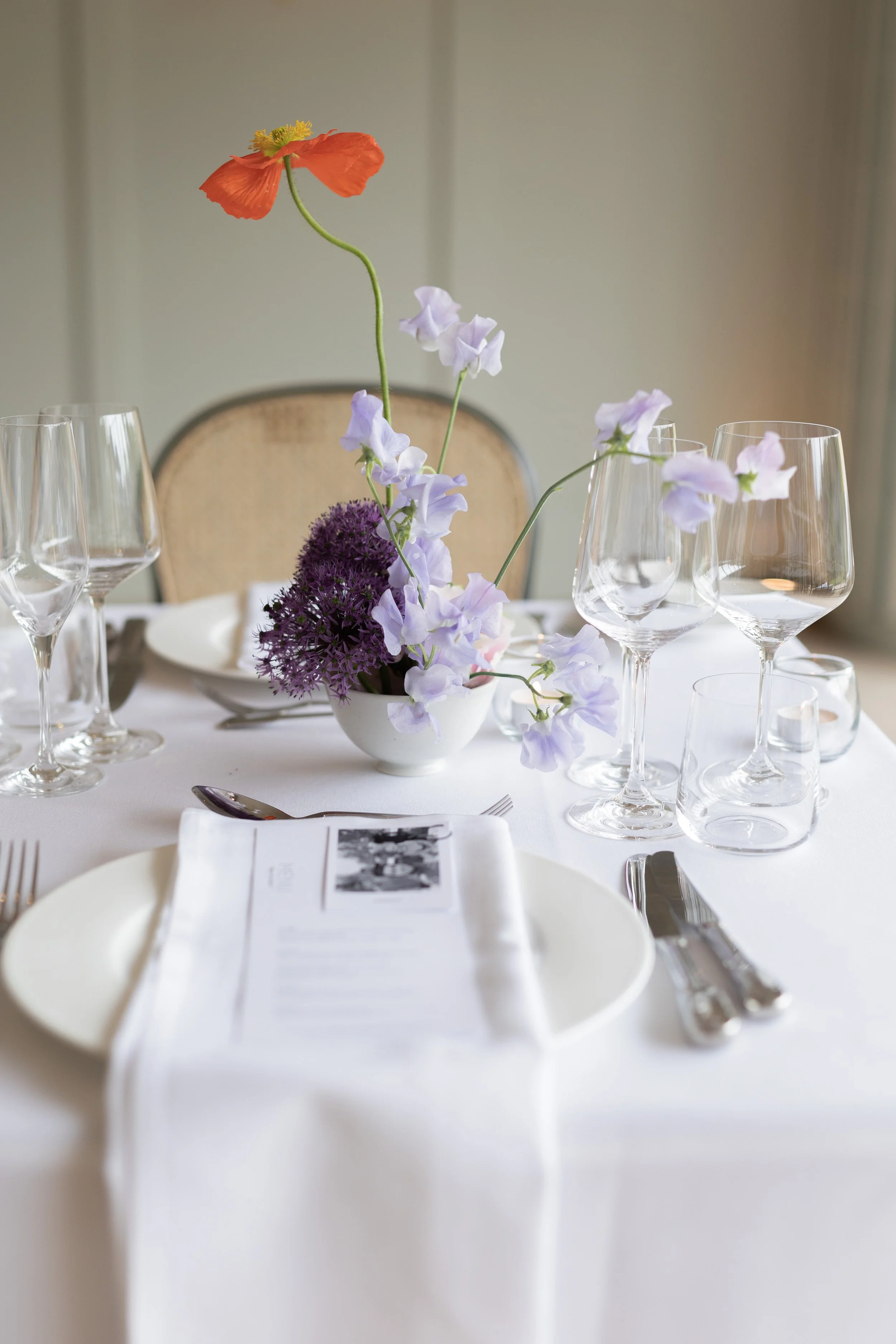 Elegant dining table set with a floral centerpiece, wine glasses, and silverware, in a well-lit room.